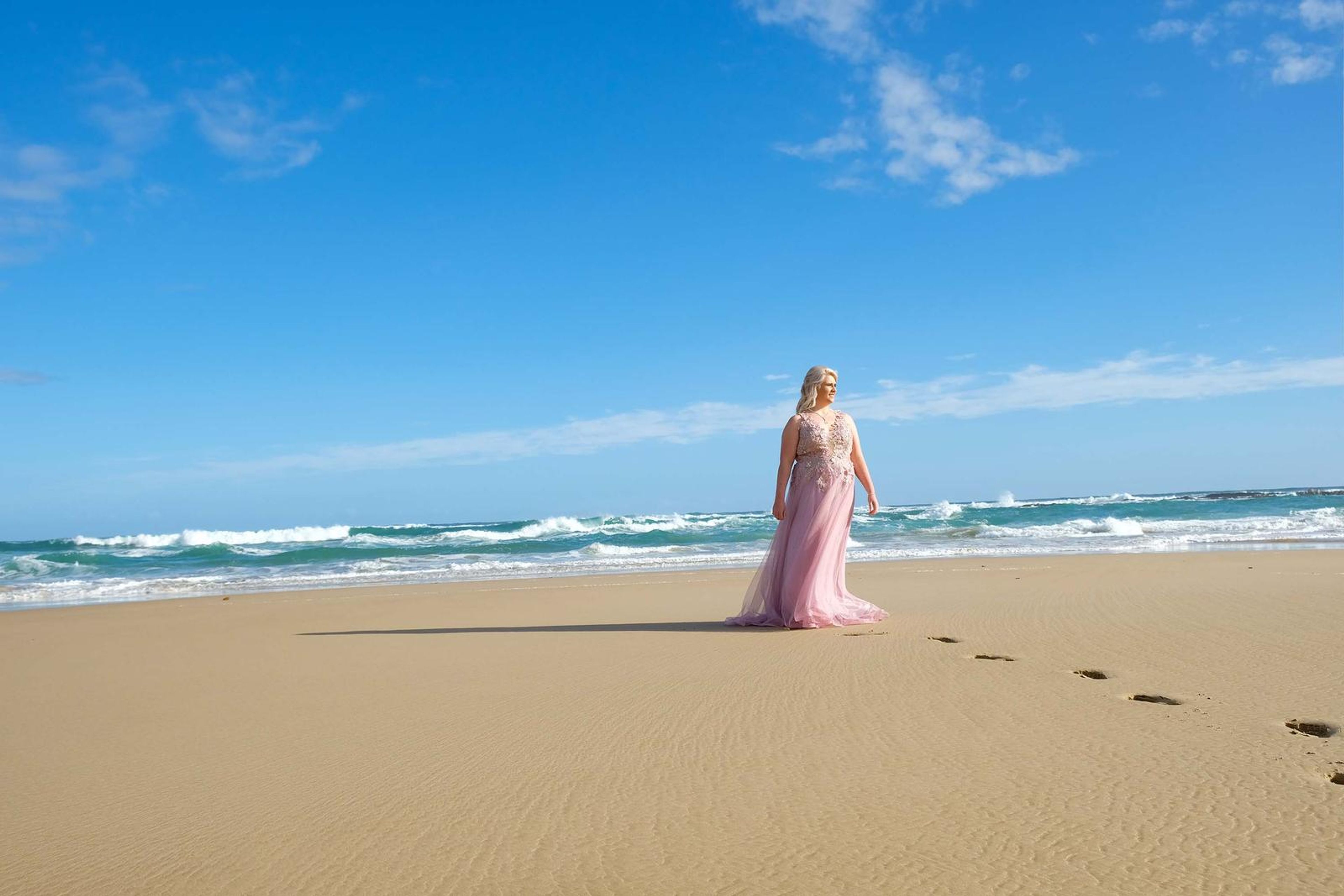 Walking along the shoreline in the pink gown, footprints behind