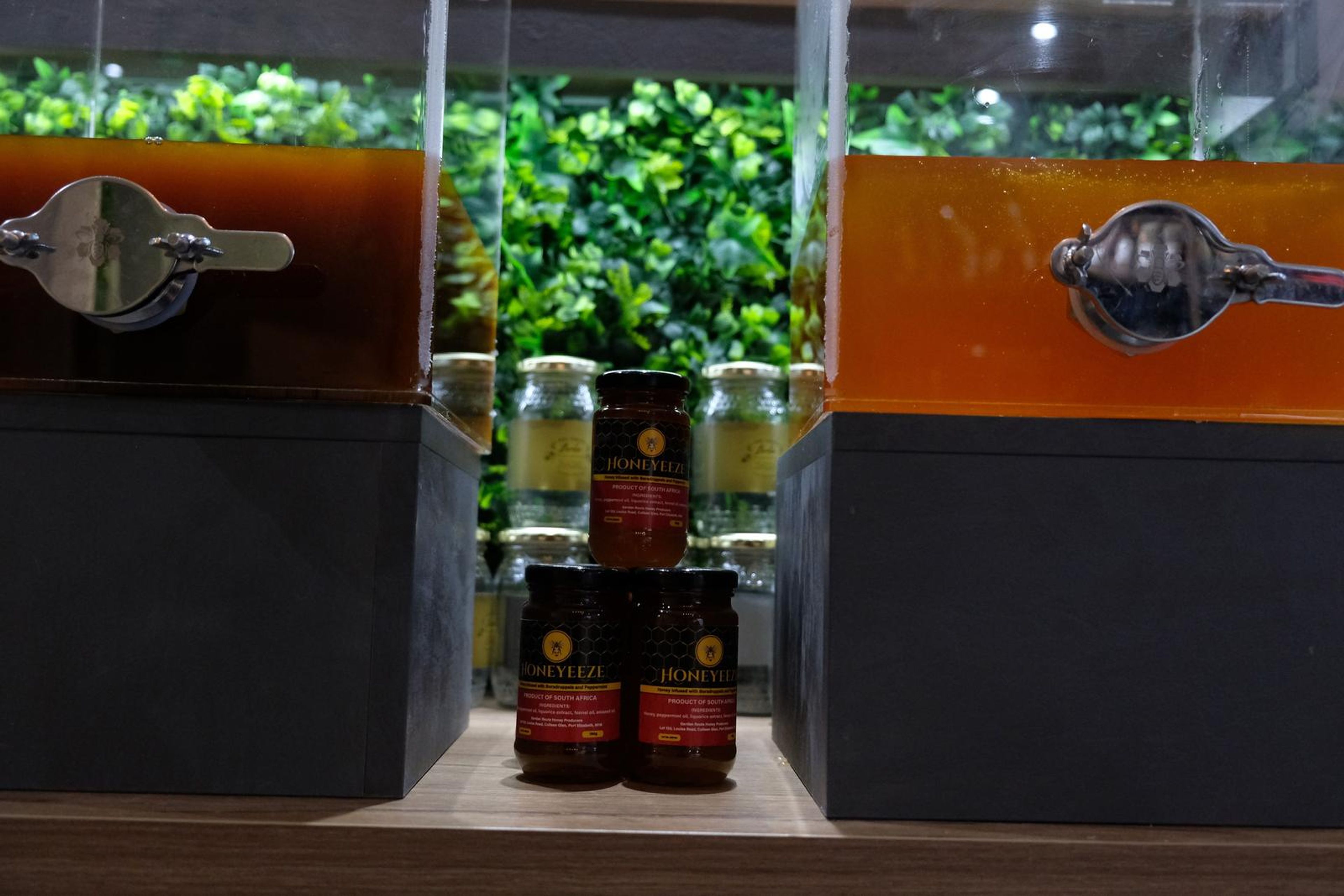 Honey dispensers with stacked Honeyeeze jars between them in front of a green wall