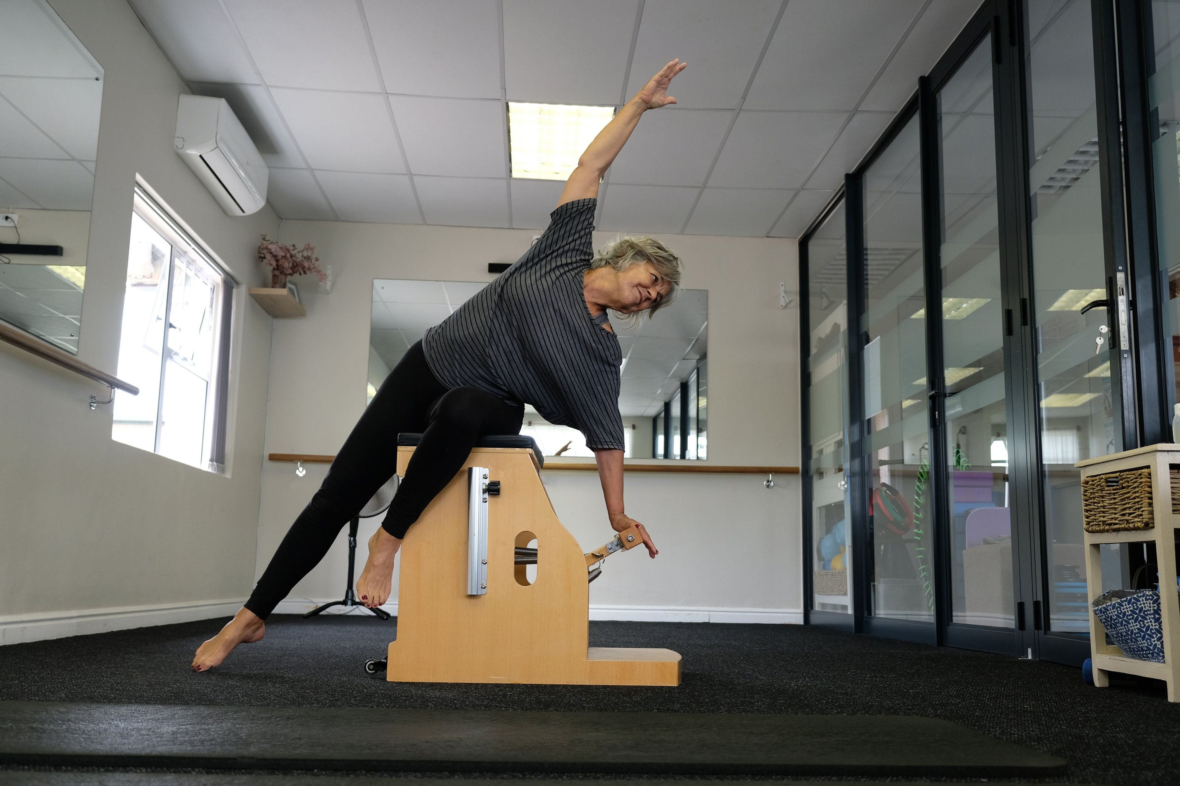 Instructor in a side stretch on a wooden Wunda chair in a bright studio