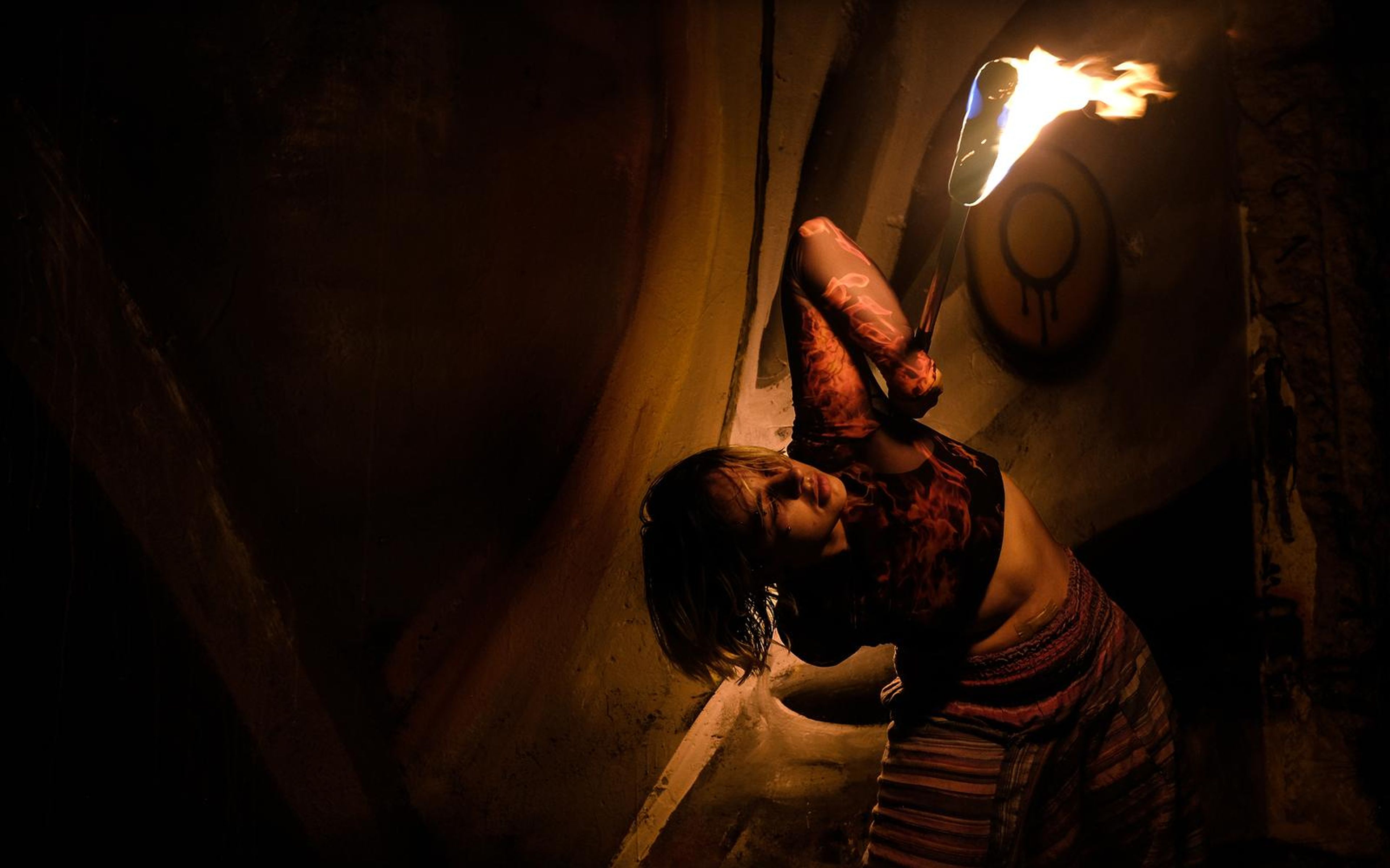 Performer bending backward with a fire staff held up toward the top right, mural behind