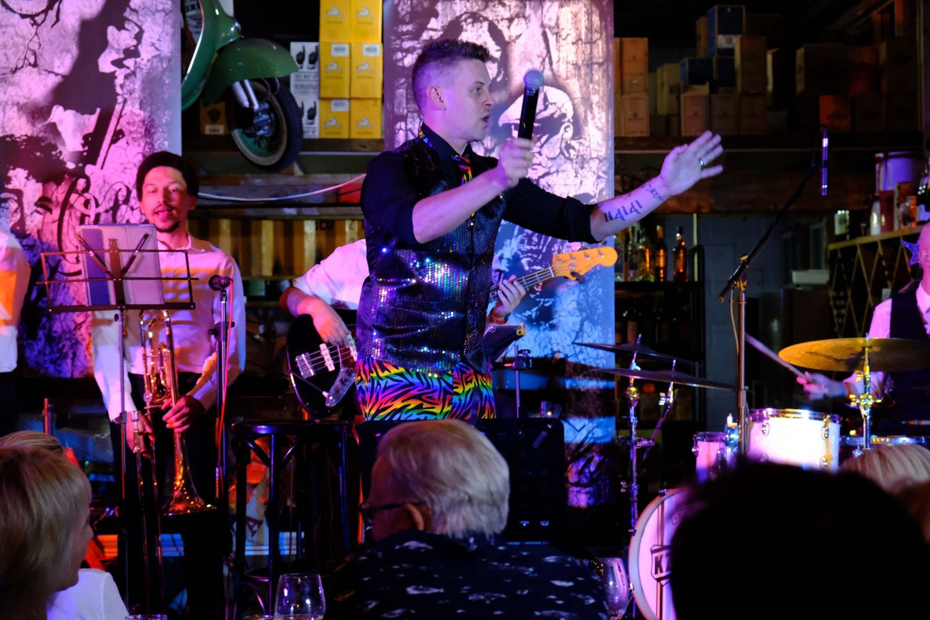 Singer in a waistcoat gesturing on stage with a mural behind him