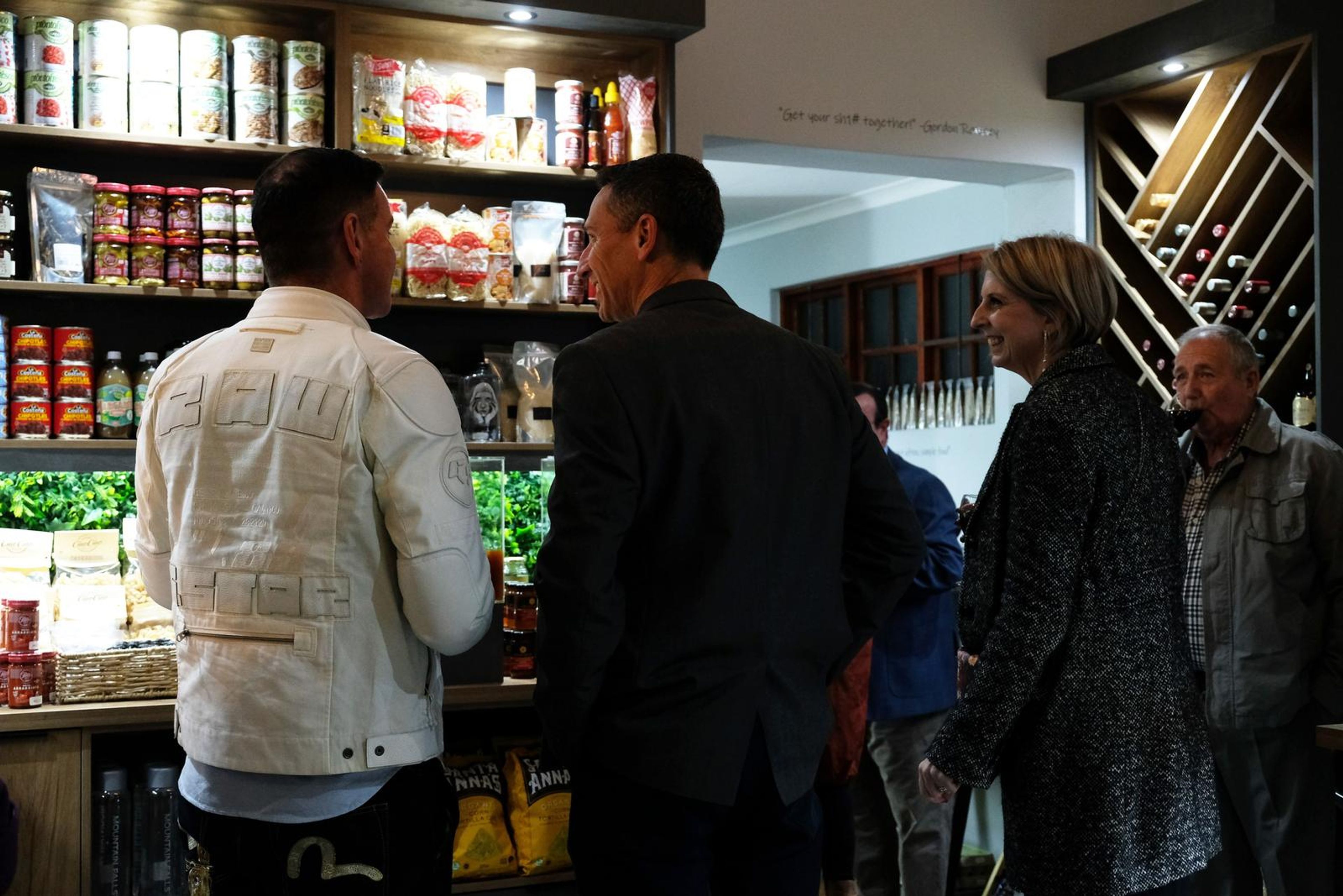 Guests chatting in front of the pantry shelves, one in a white jacket