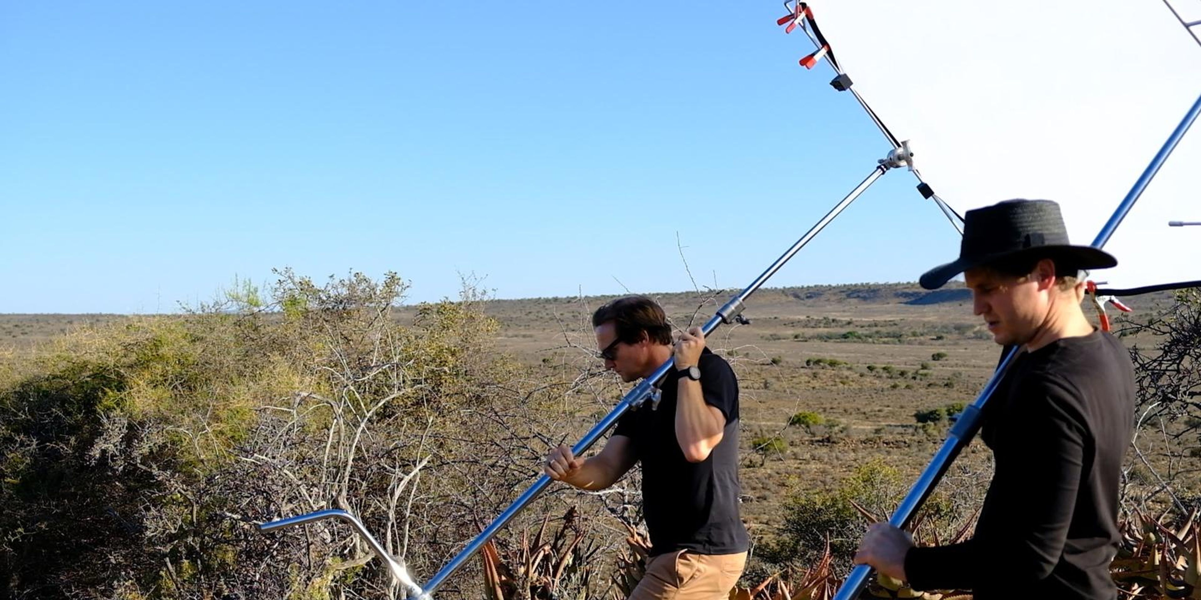 Crew members carrying a boom stand across the hill