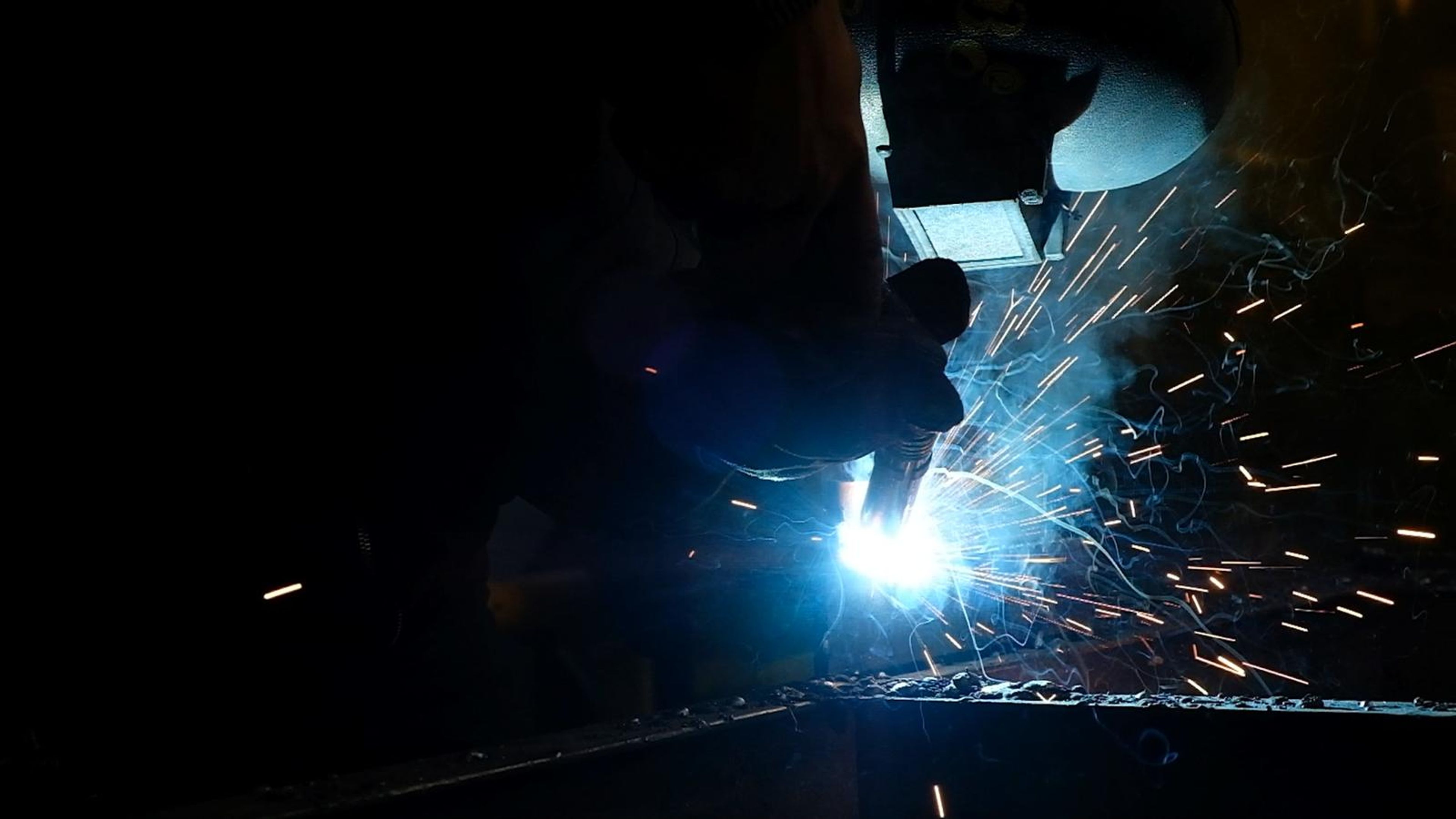 Helmeted welder in blue light with fine sparks