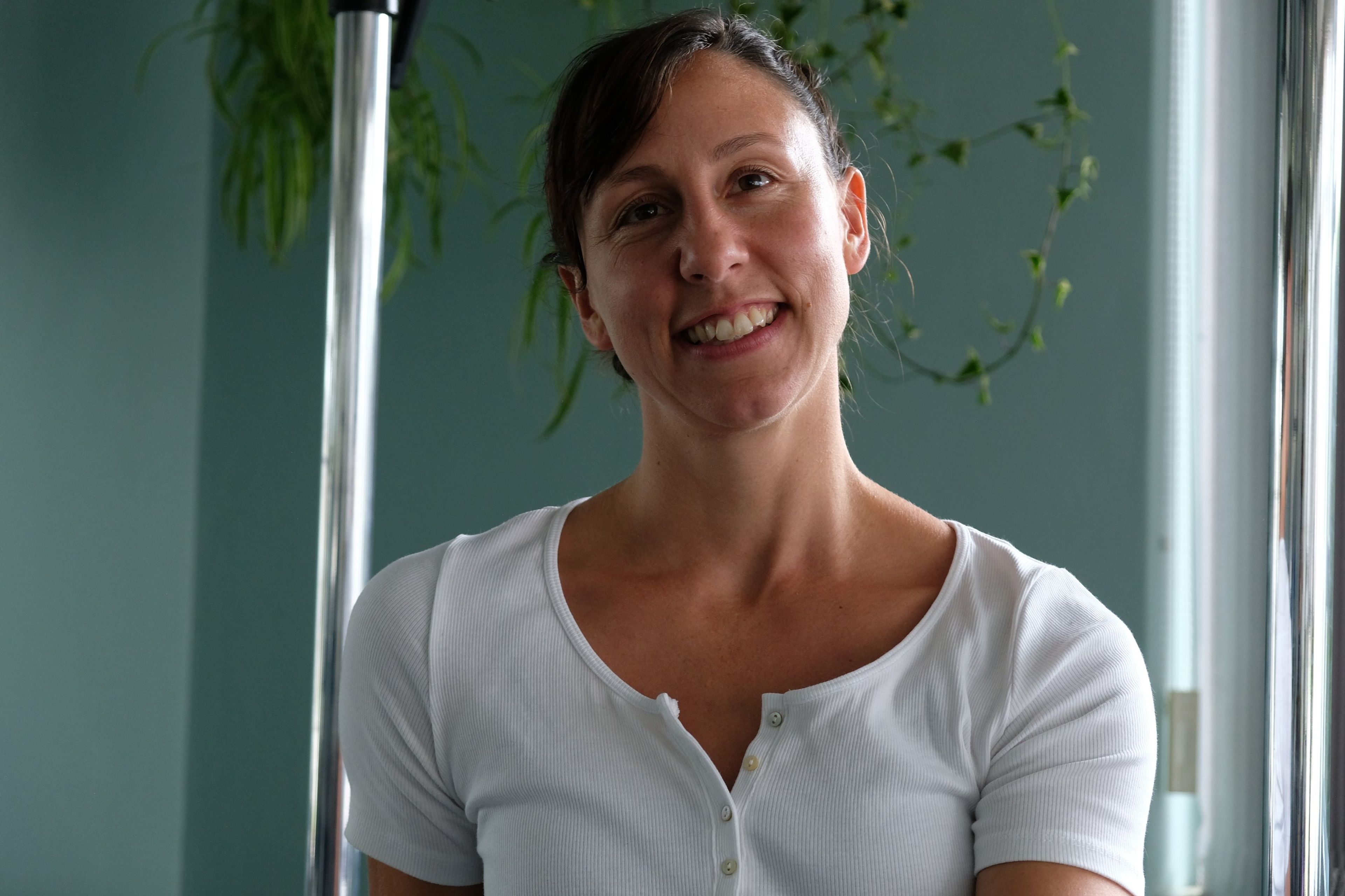 Portrait of an instructor in a white top, head tilted and smiling, studio equipment behind her