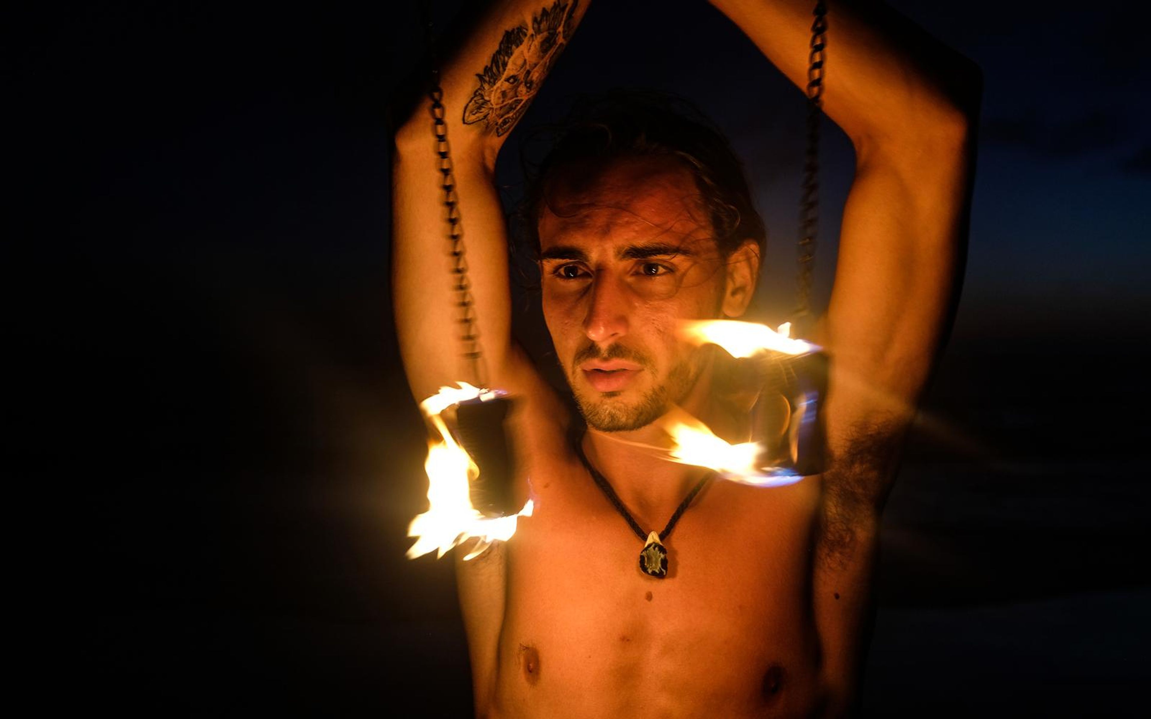 Close-up of a man wearing a pendant with arms raised and chains of fire hanging at both sides