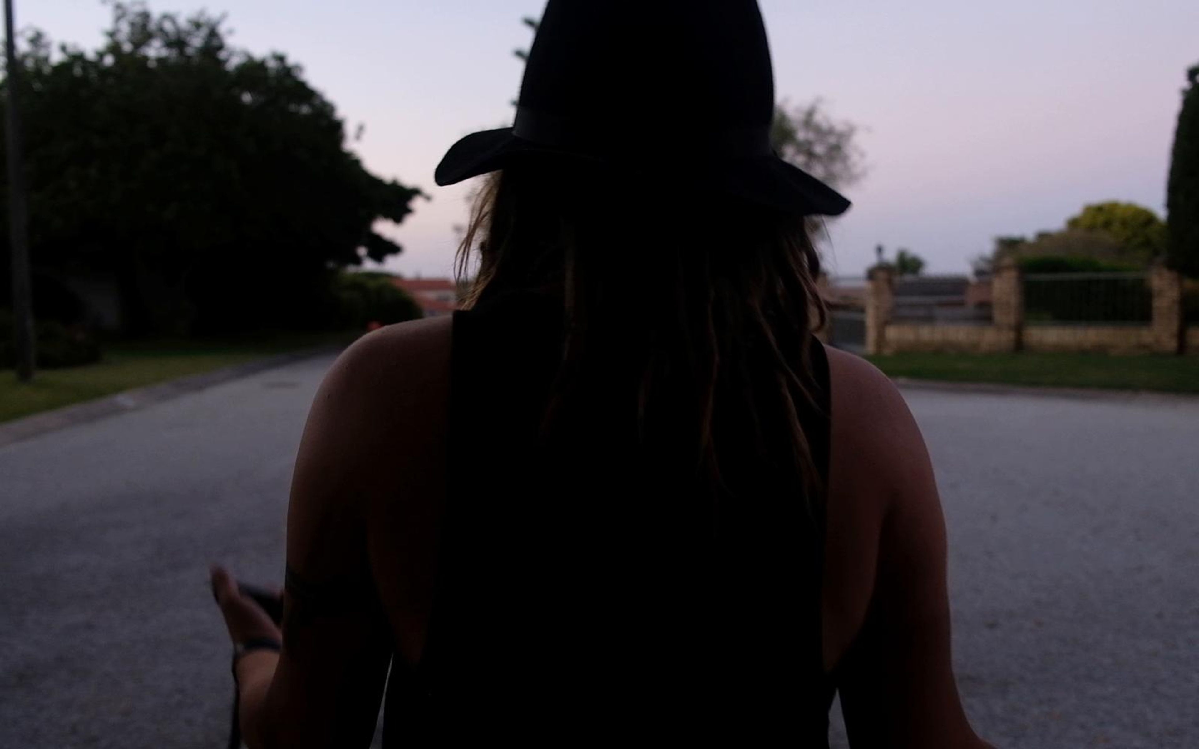 Fire performer seen from behind in a dark cap with long dreadlocks on an empty road at dusk