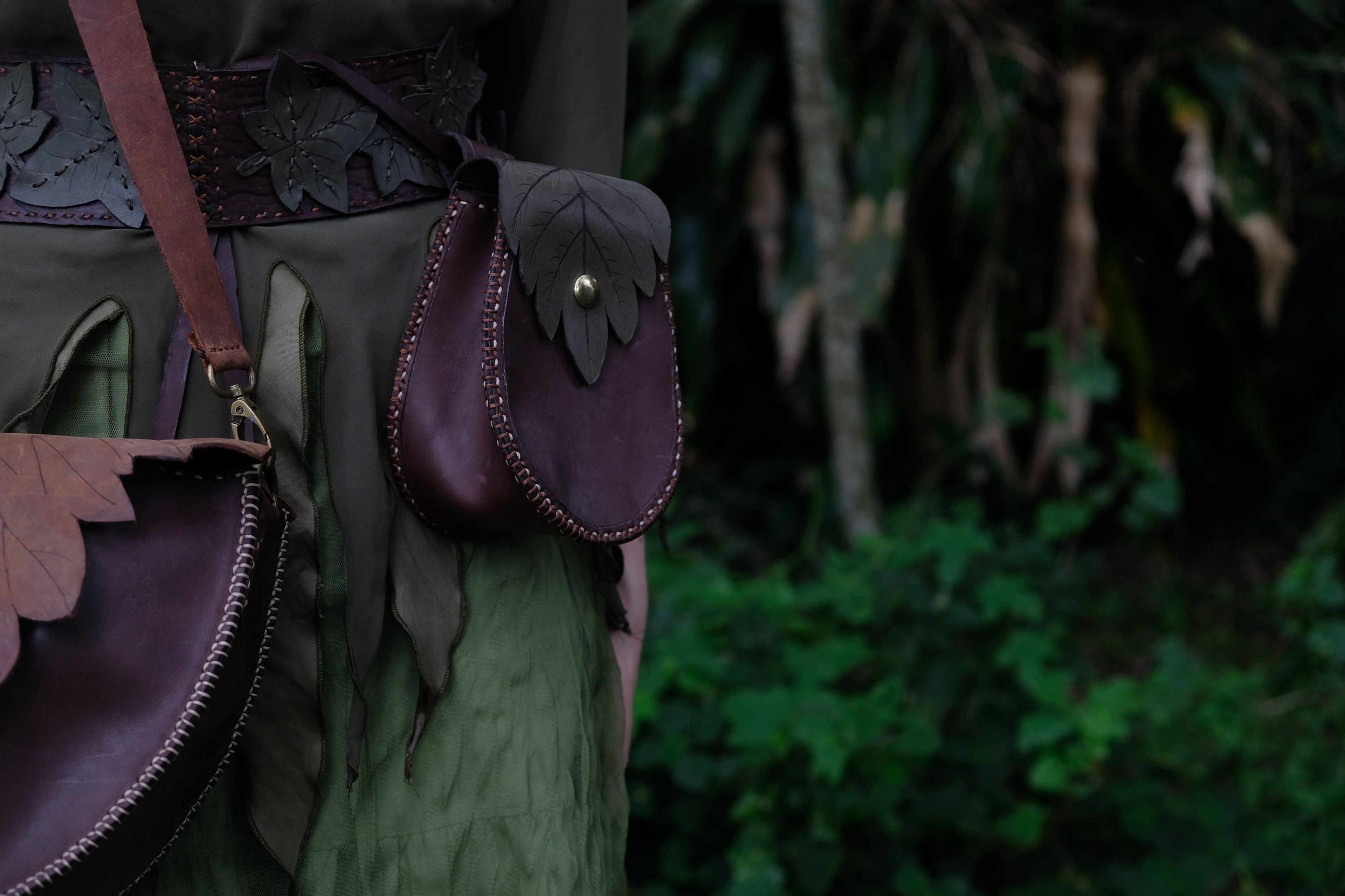 Purple-brown leather pouch with a leaf flap on a belt over a green dress