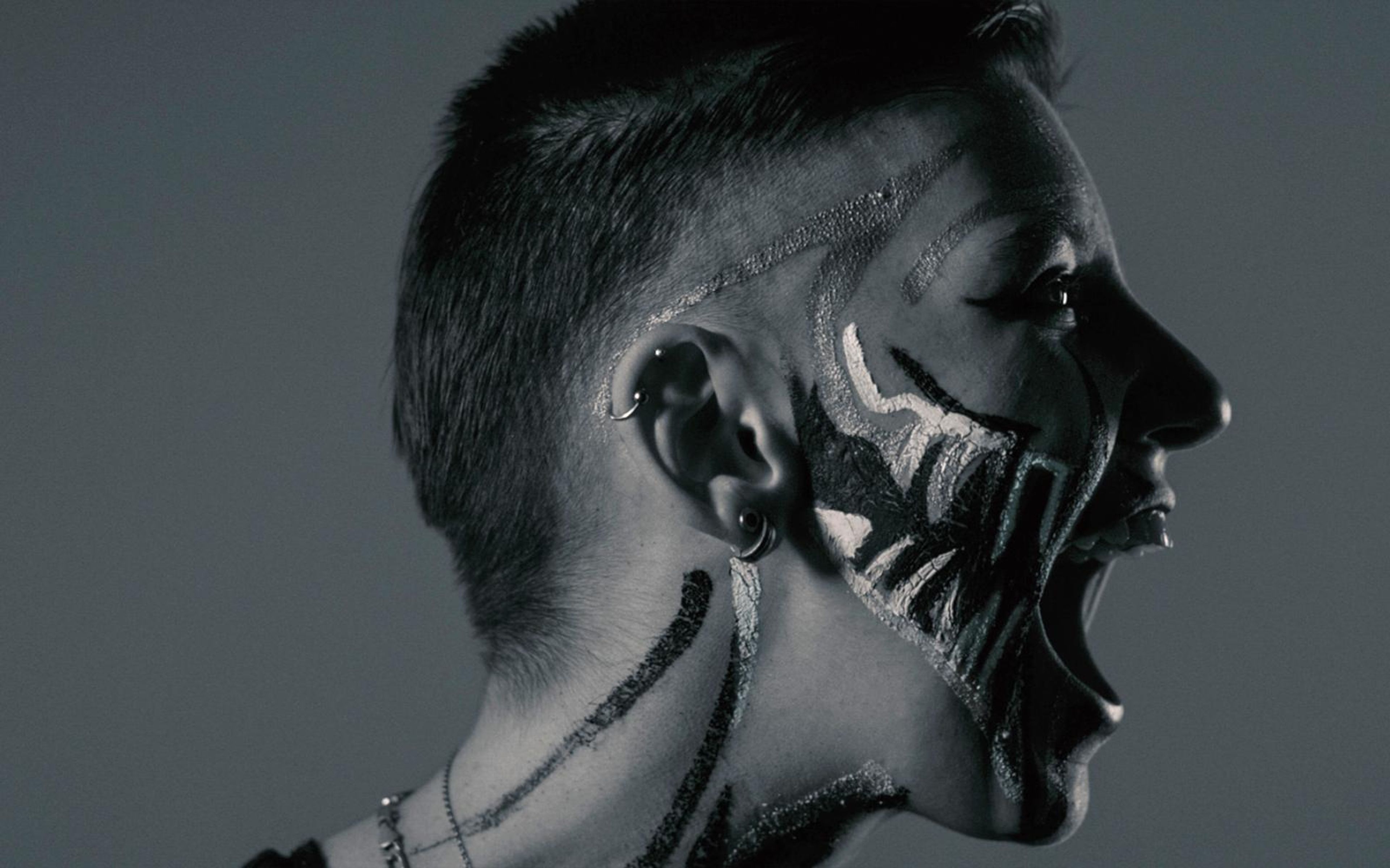 Black and white portrait of a performer screaming in profile, face paint streaked across the cheek and neck
