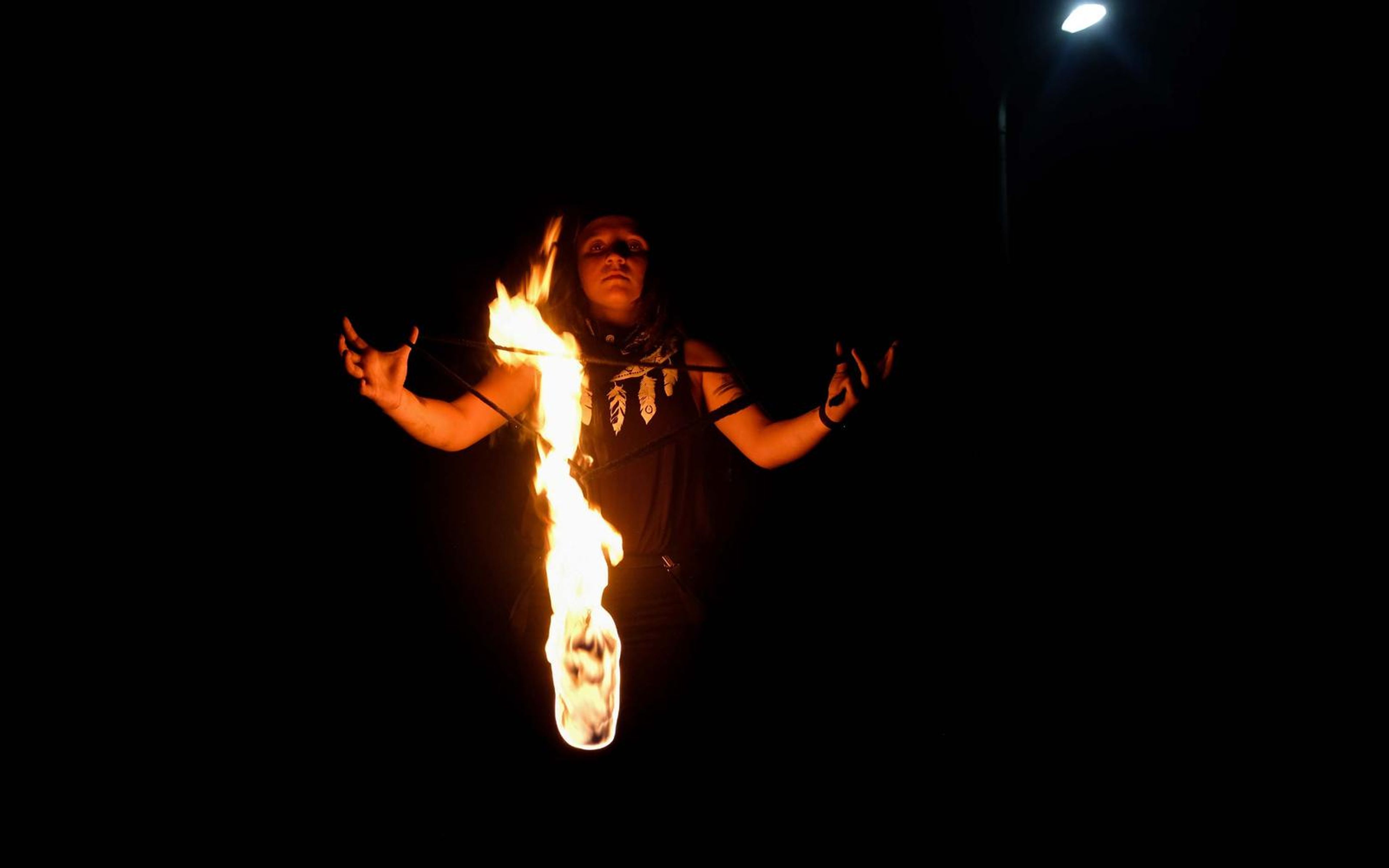 Small figure with outstretched arms behind a long vertical flame, a street light at top left