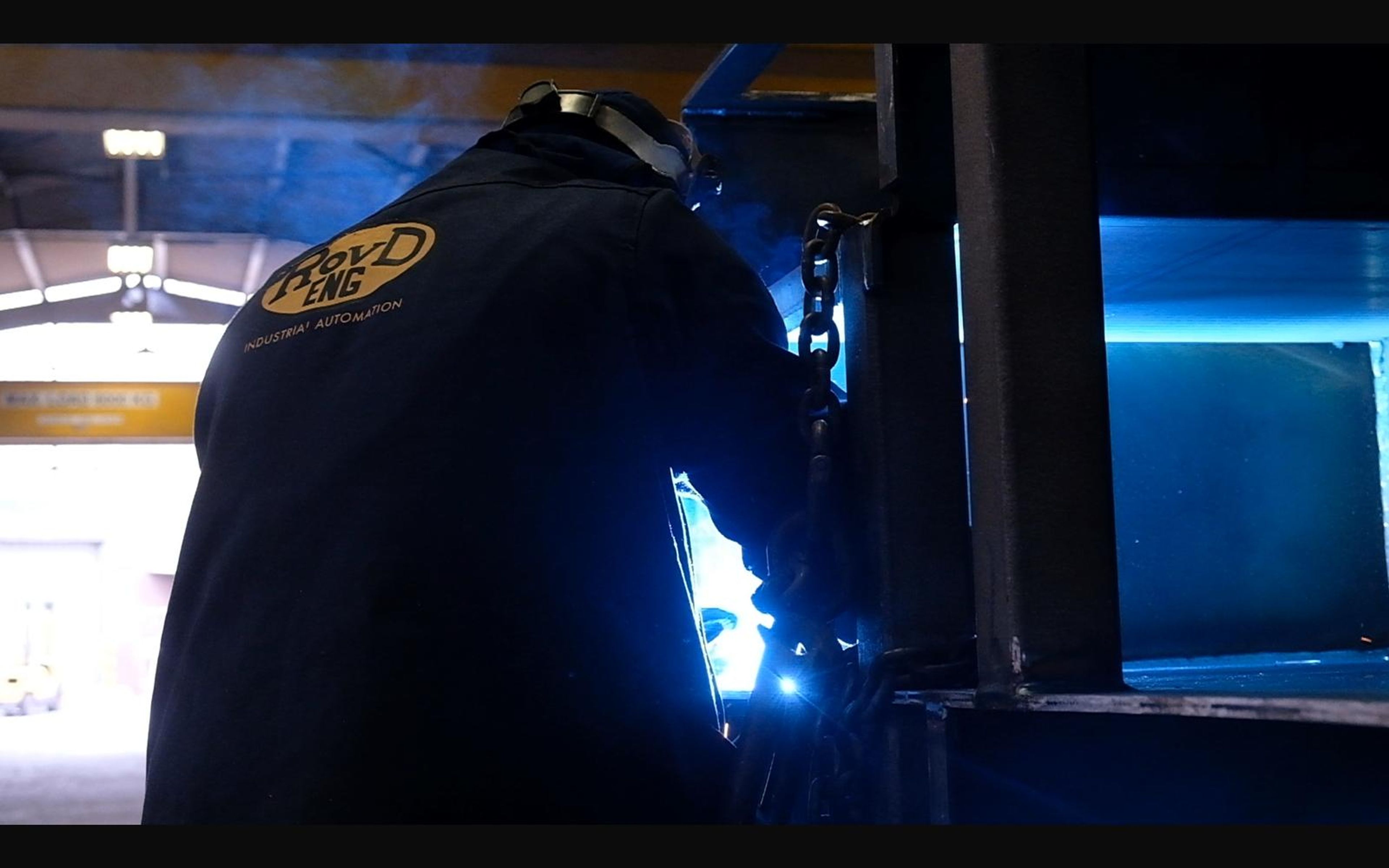 Welder in a dark jacket welding in blue light