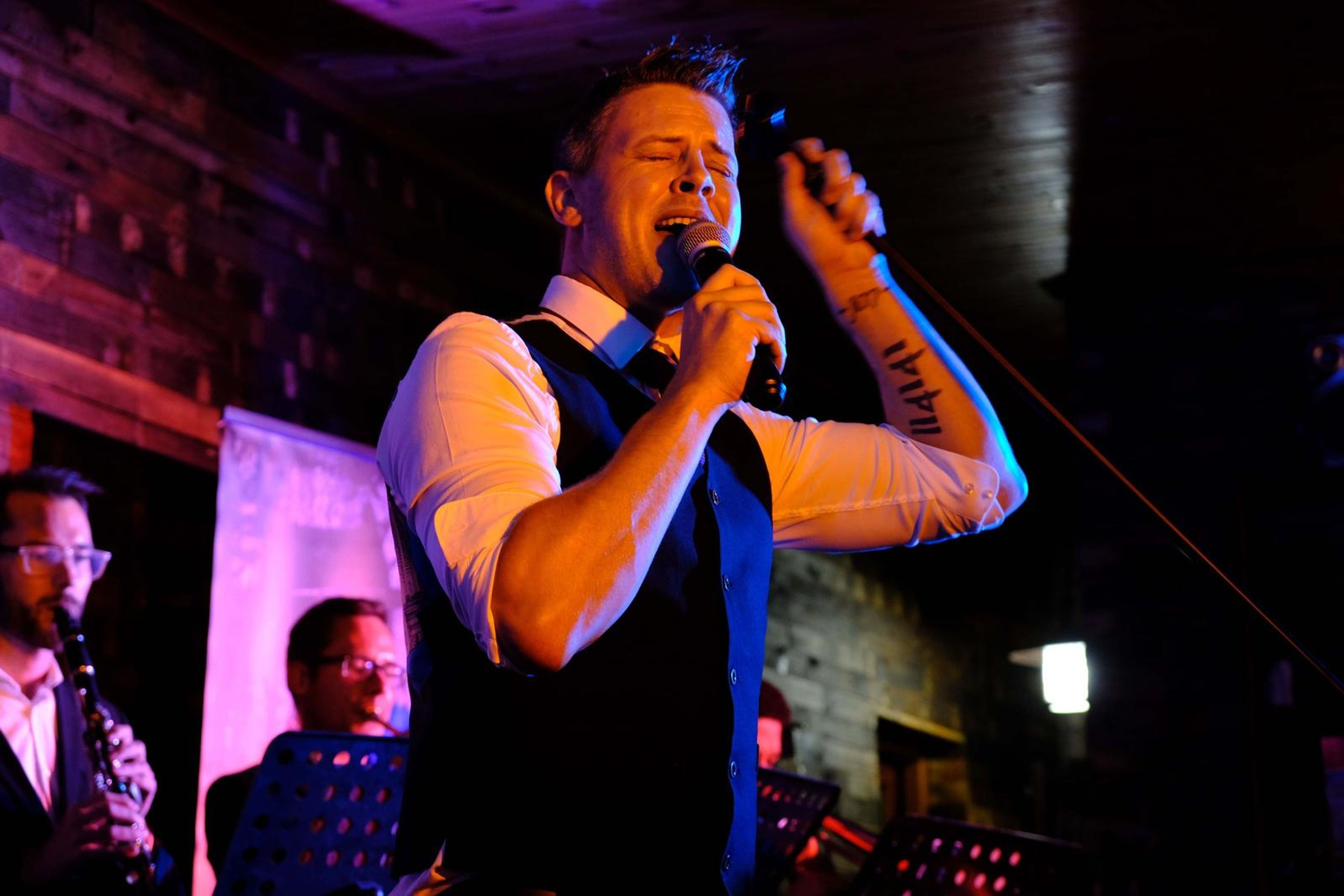 Singer in a waistcoat singing with his tattooed arm raised