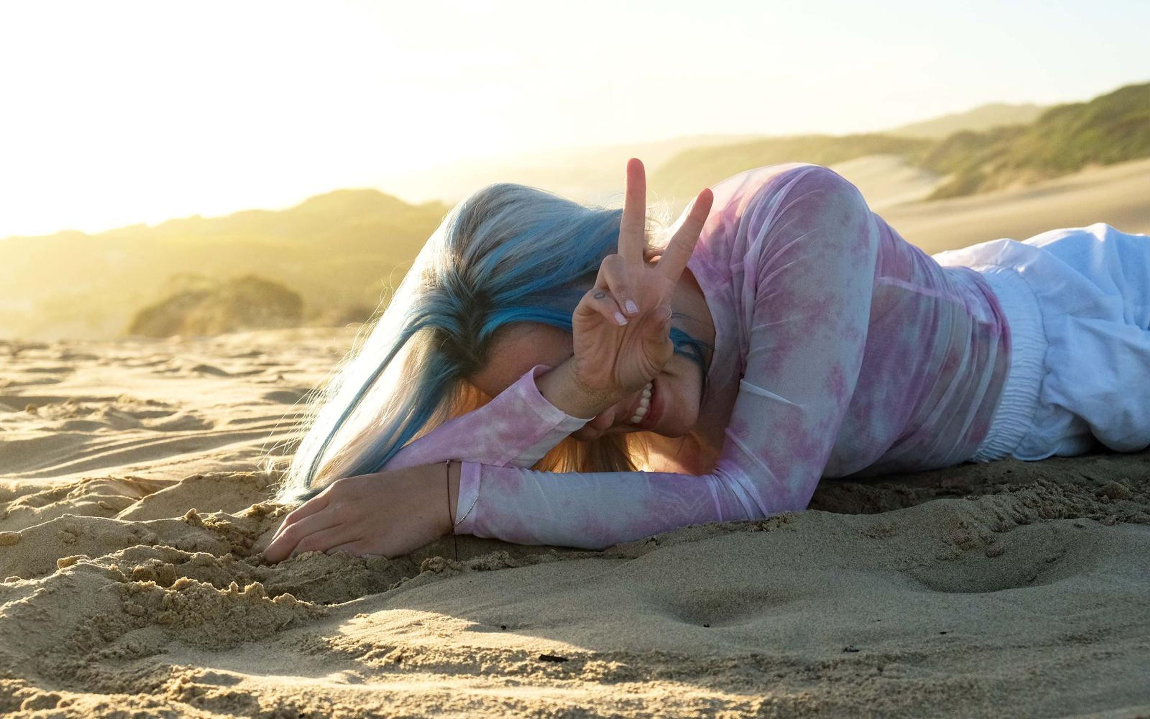 Woman lying on the sand with fingers making a peace sign beside her face