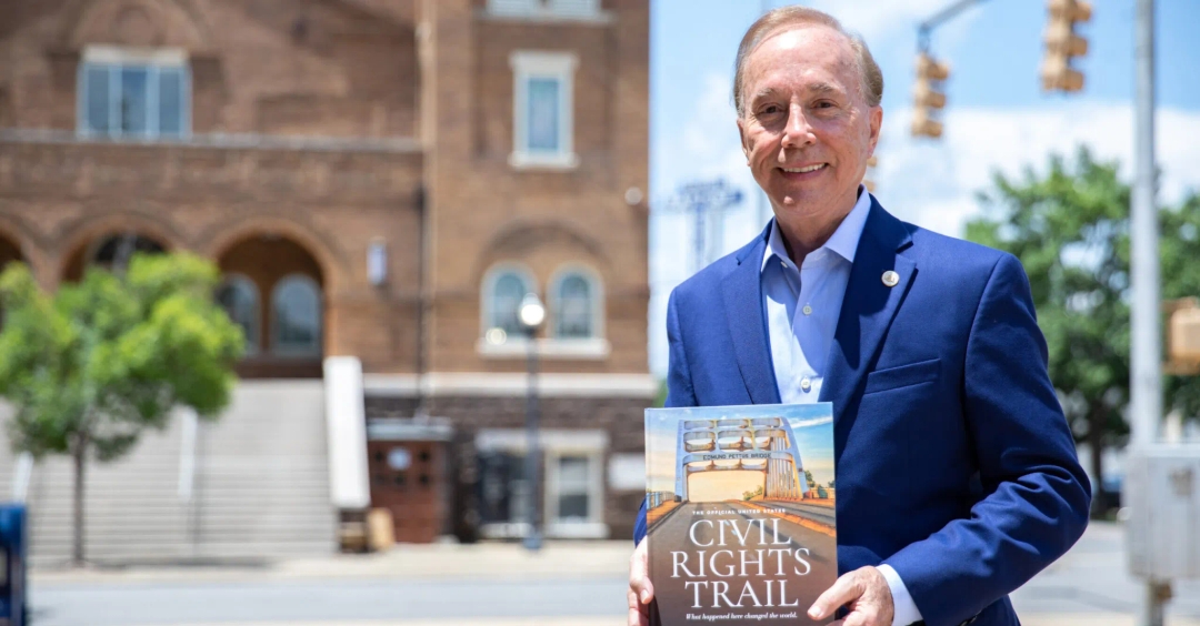The Director Lee Sentell is outside is holding a book titled "The Official United States Civil Rights Trail.