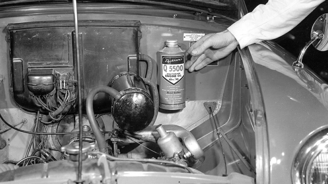 A hand pouring oil from a Duckhams can into an open engine bay.