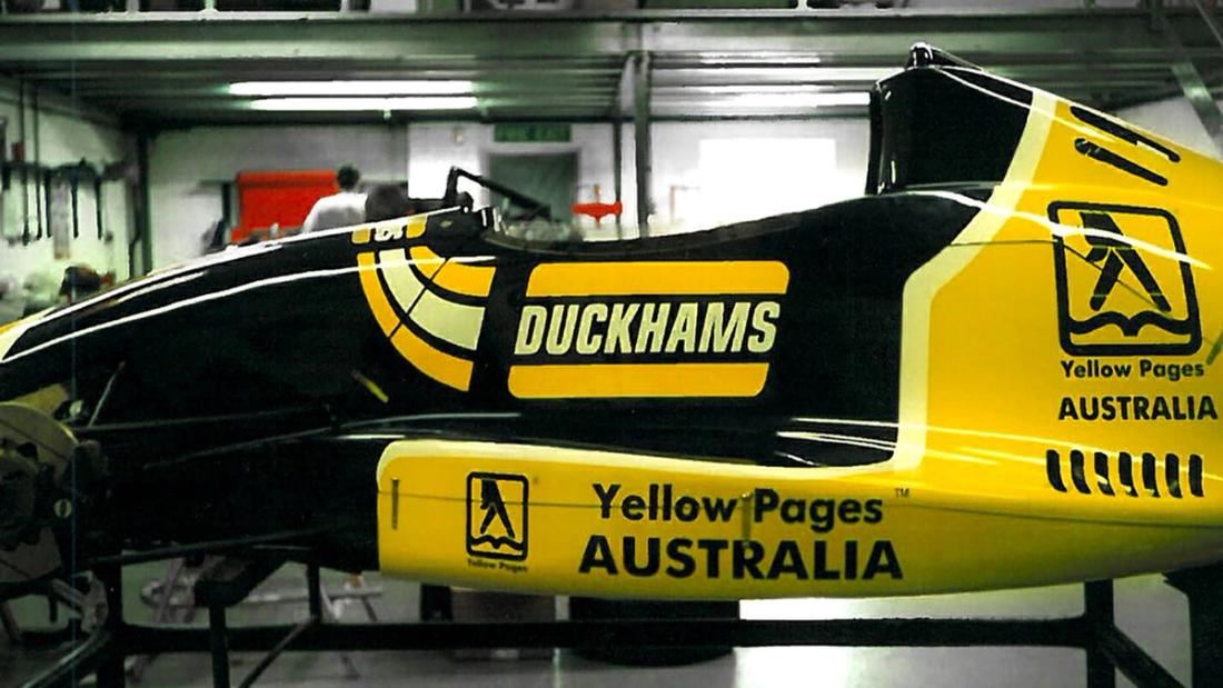 A yellow Duckhams and Yellow Pages Australia single-seater racing car in a garage.