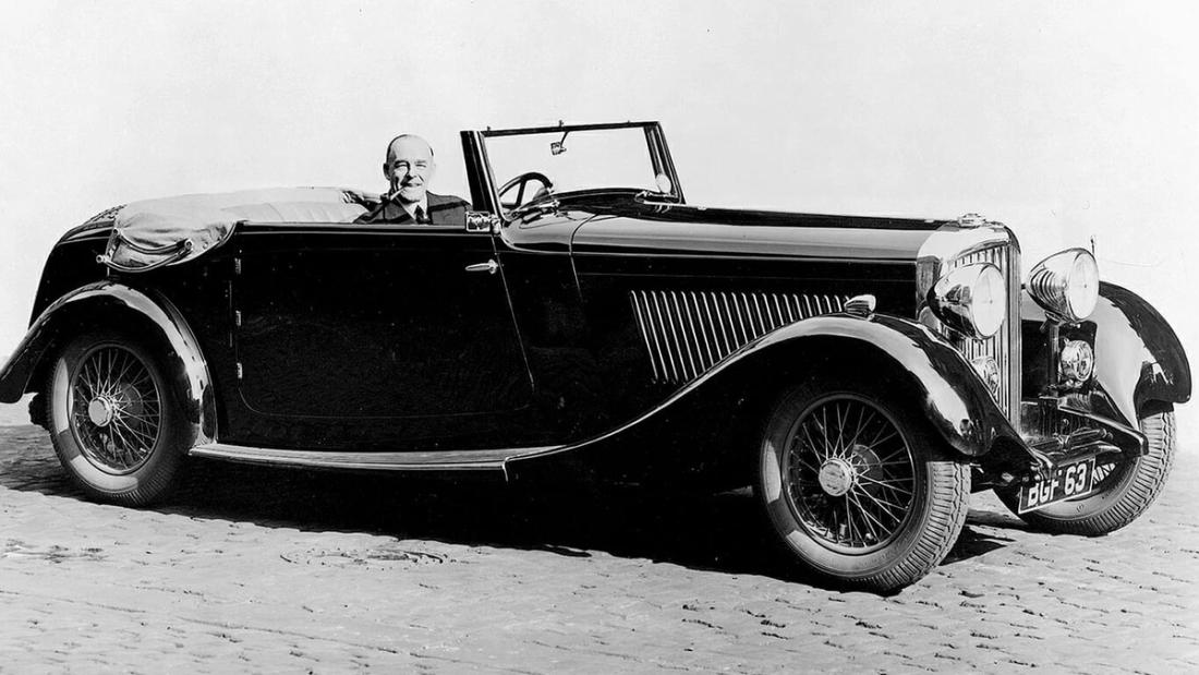 A 1930s open-topped sports car being driven across flat open sand.