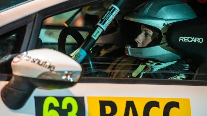 A driver in helmet and race suit at the wheel of a car marked 63.