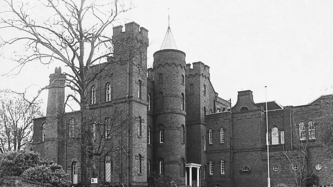 Vanbrugh Castle in Greenwich: a castle-style brick house with battlements and a round tower with a pointed roof, behind a brick wall.