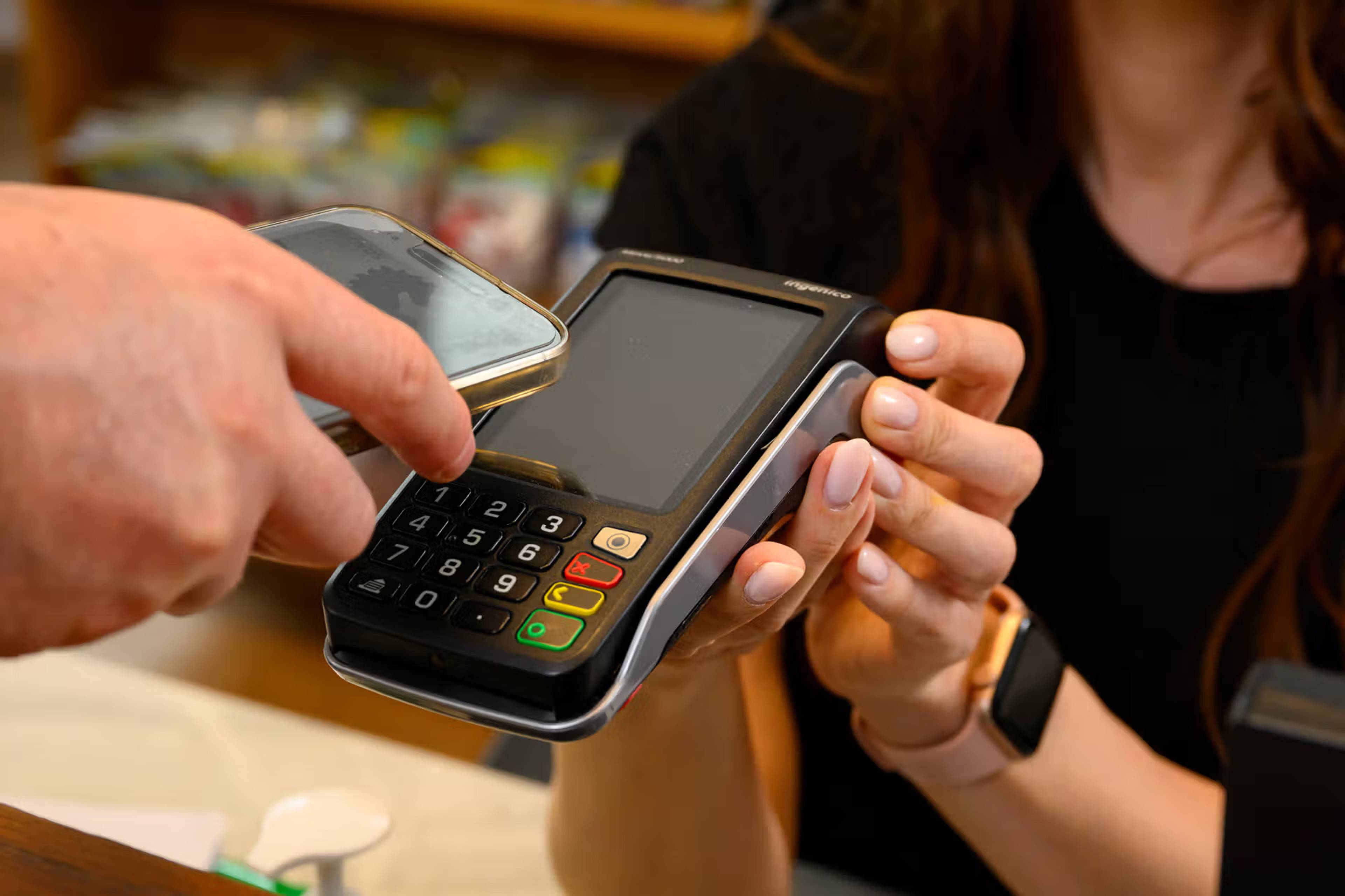 Person making a contactless payment using a smartphone at a card payment terminal held by a reception team member.