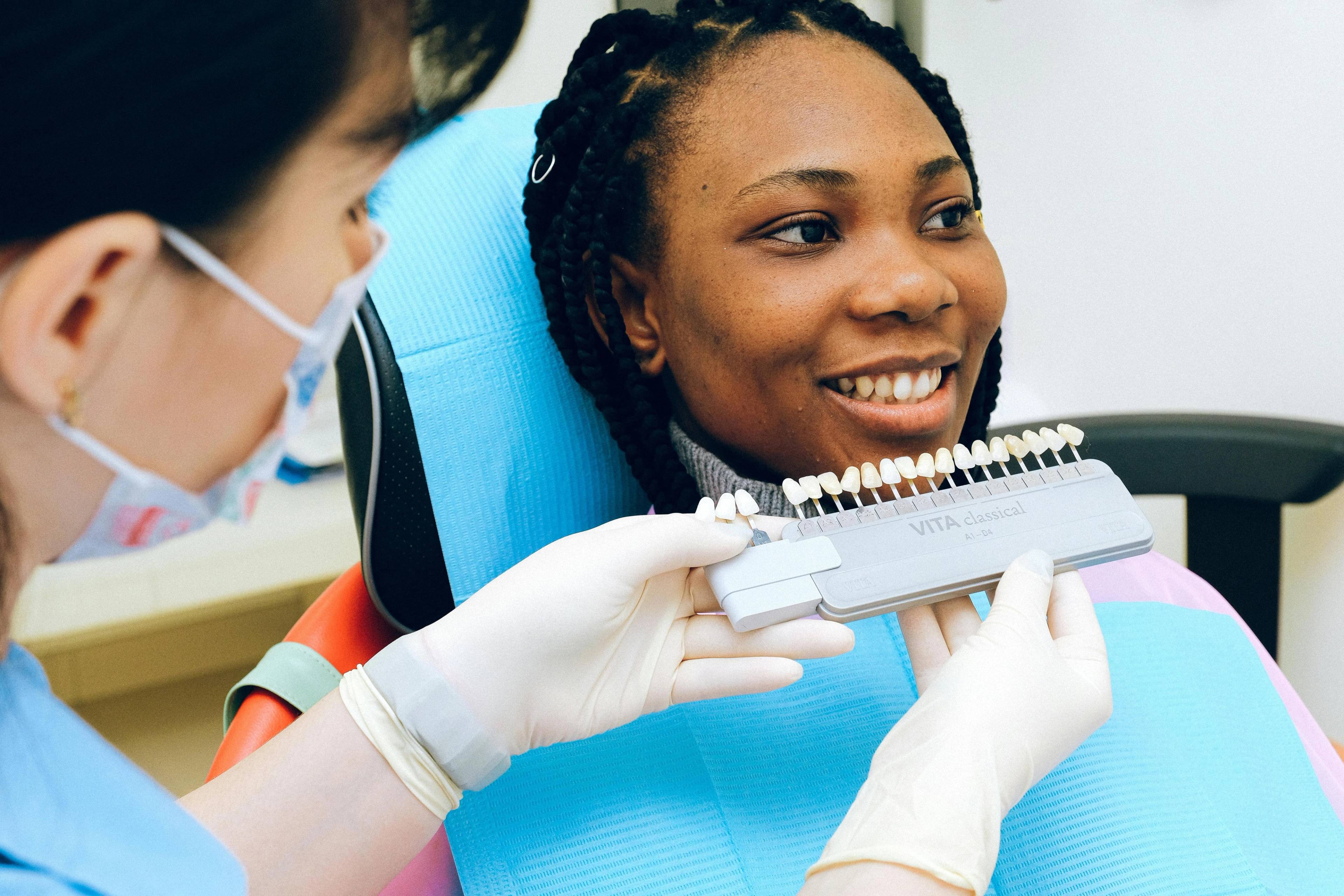 Dental professional matching a patient's tooth shade using a dental shade guide during a cosmetic dentistry consultation.