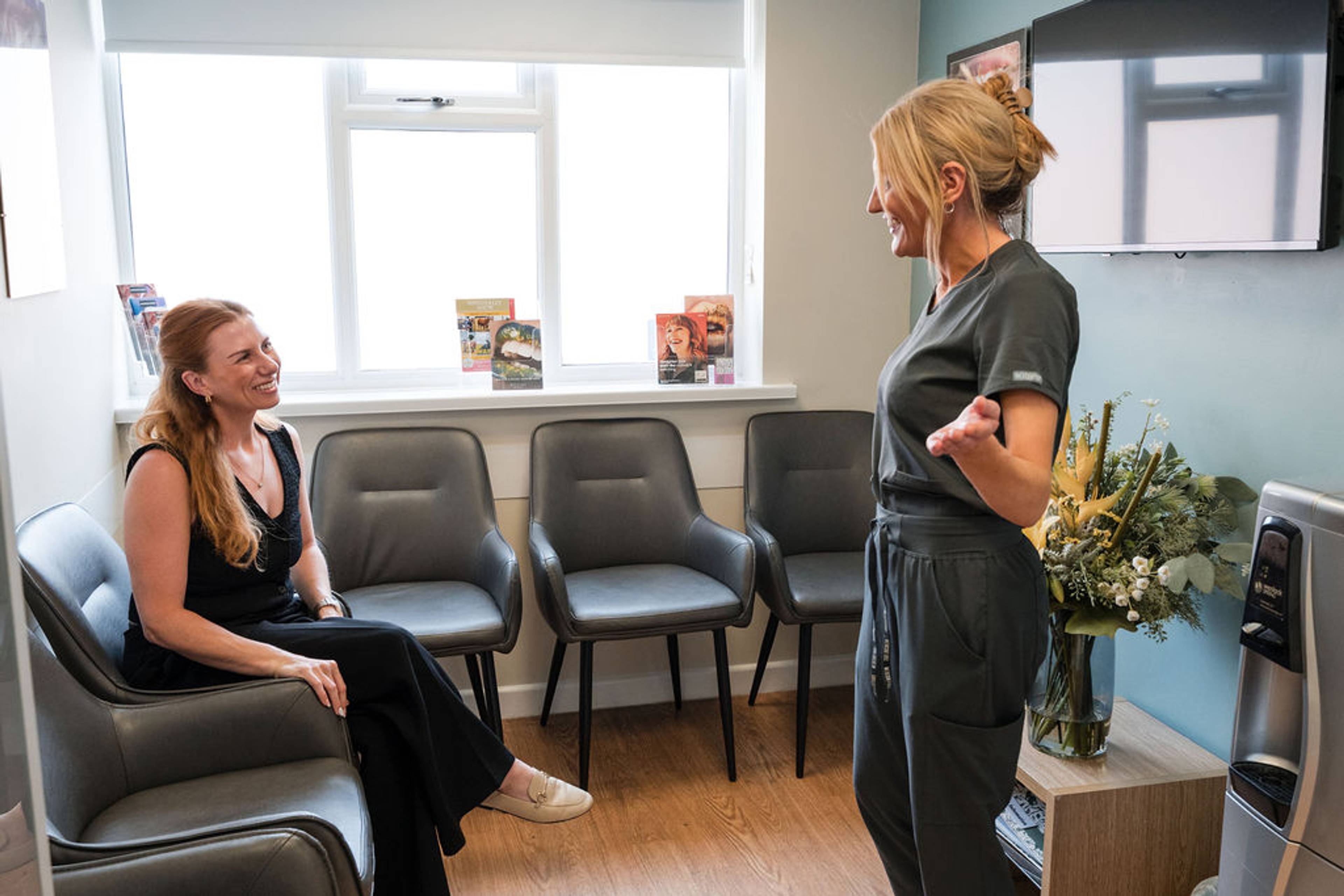 Dental team member speaking with a patient in a welcoming dental clinic waiting area.