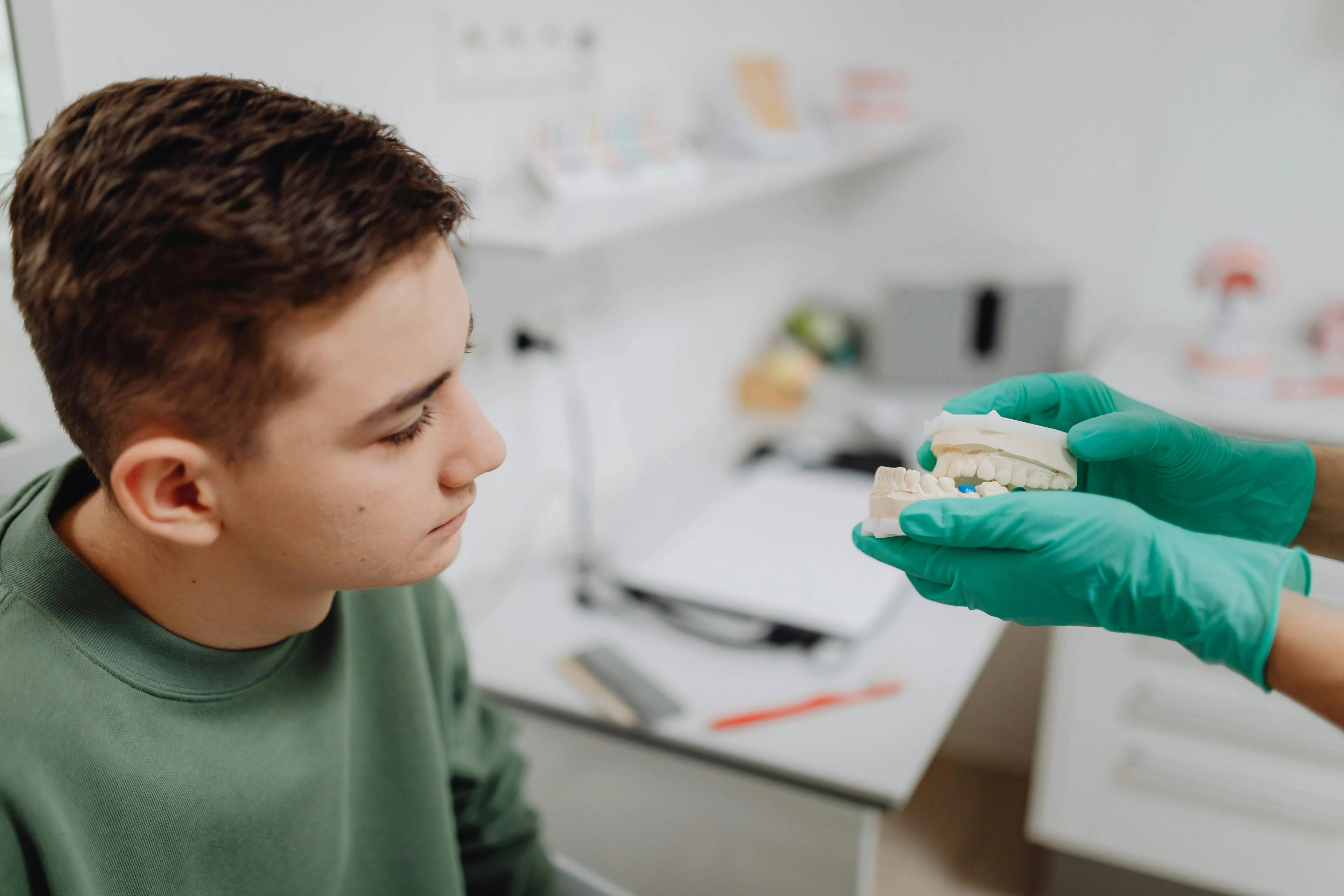 Dental professional using a tooth model to explain oral health or orthodontic treatment to a young patient during a consultation.