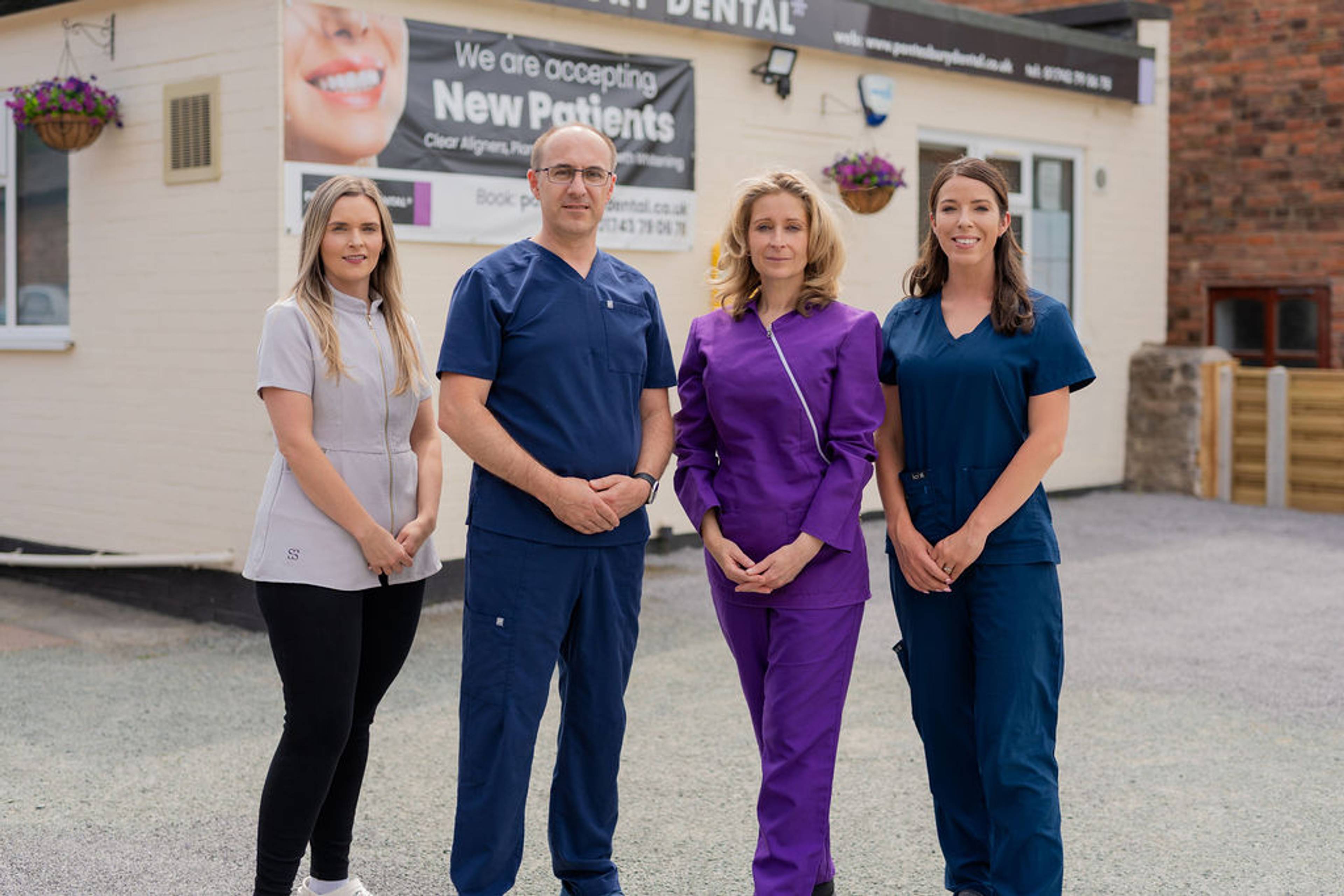 Four dental practice team members standing outside a dental clinic building in professional clinical uniforms.