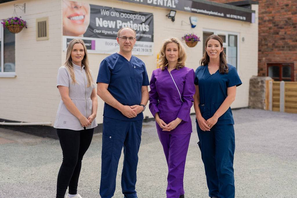 Four dental practice team members standing outside a dental clinic building in professional clinical uniforms.