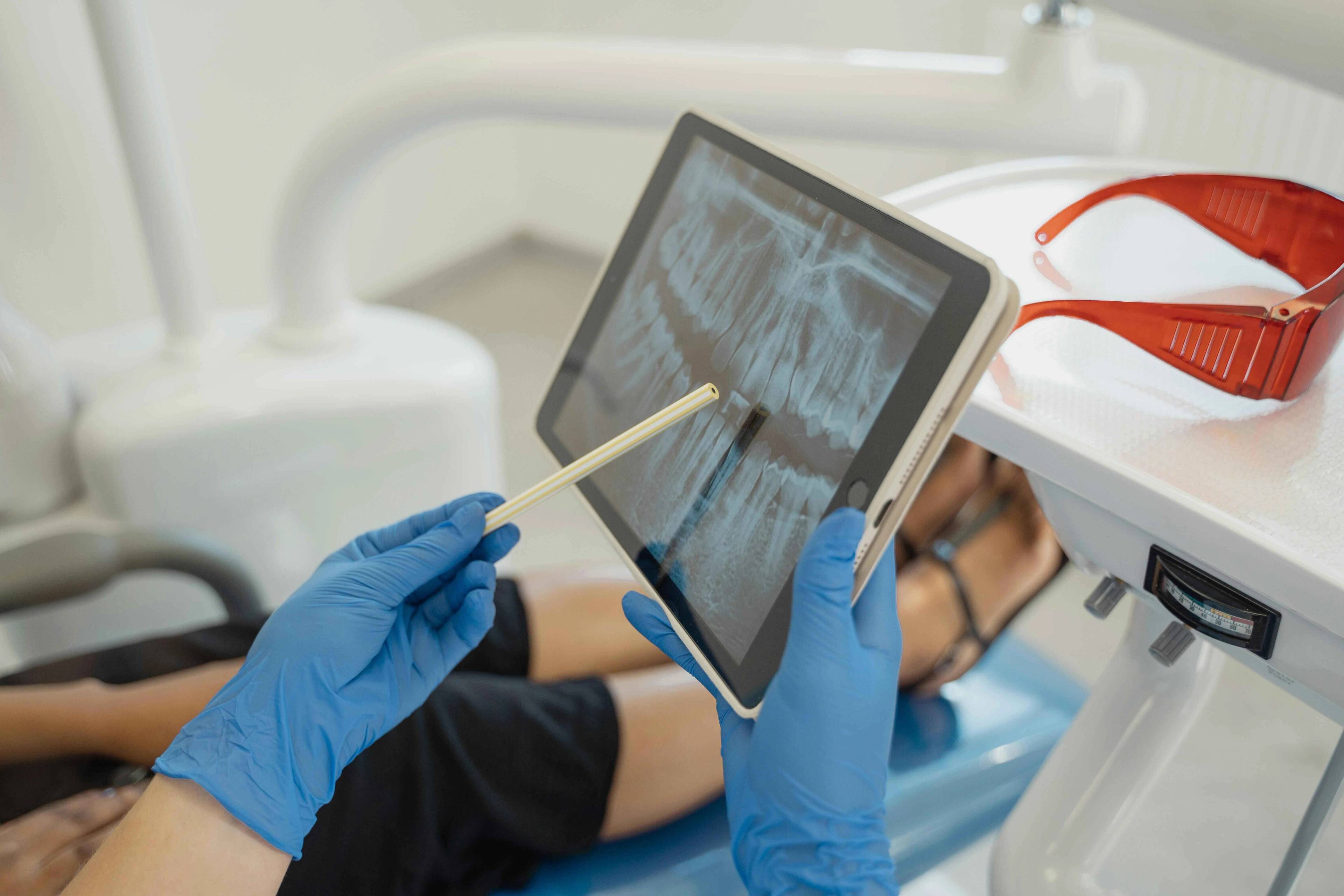 Dental professional reviewing a patient's dental X-ray on a tablet during a consultation in a treatment room.