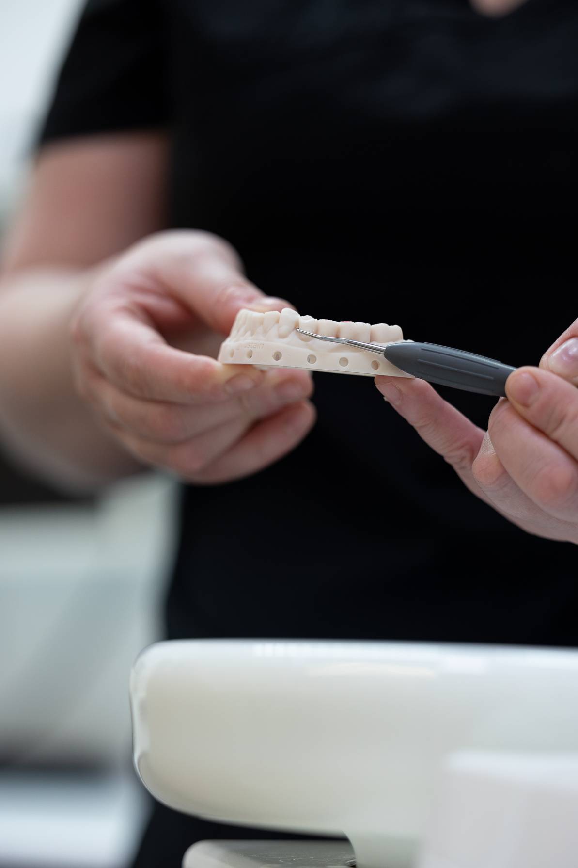 Close-up of a dental professional holding a dental model and pointing to a tooth with a dental instrument during a patient consultation.