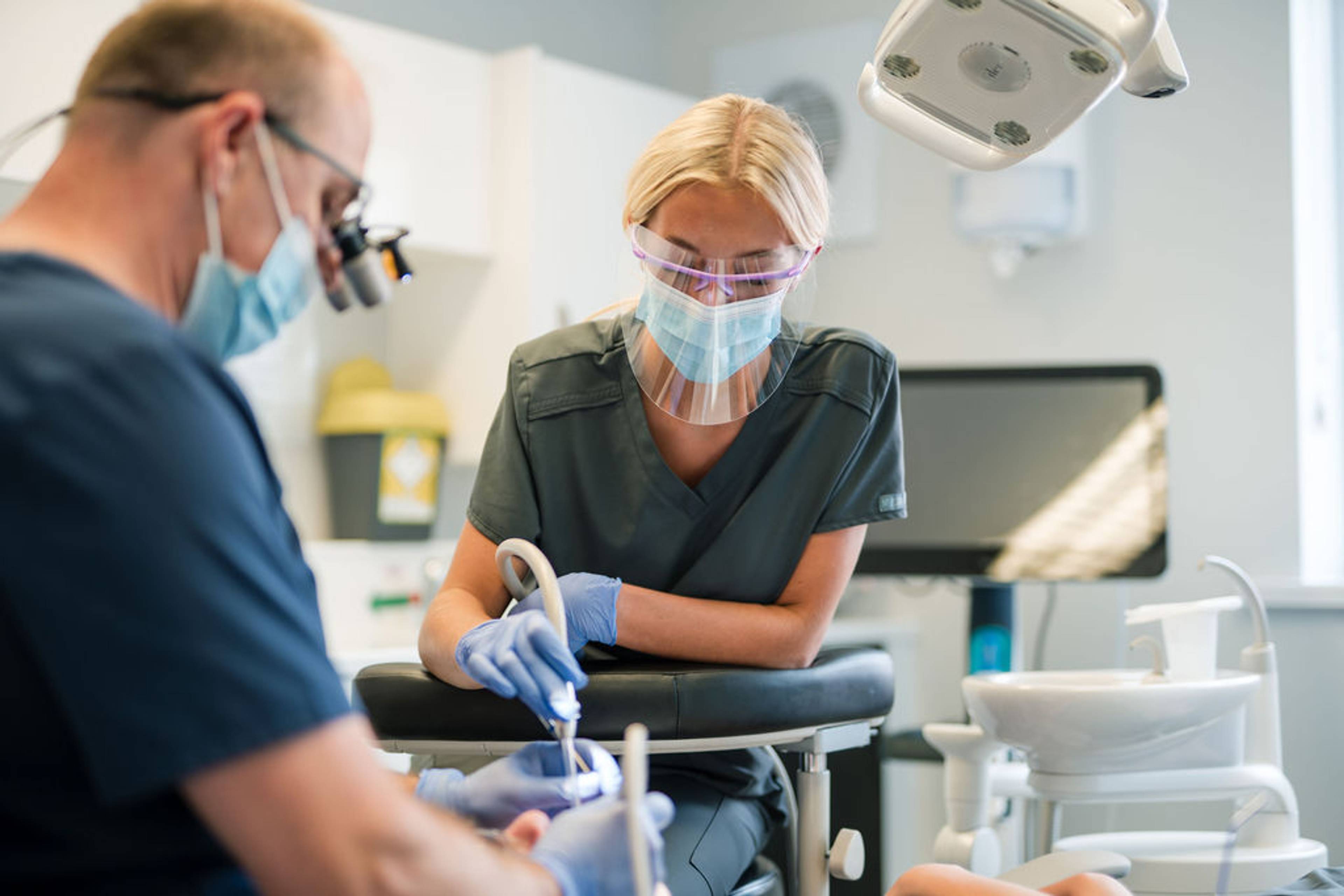 Dental professionals using protective equipment and suction instruments while providing treatment to a patient in a modern dental surgery.