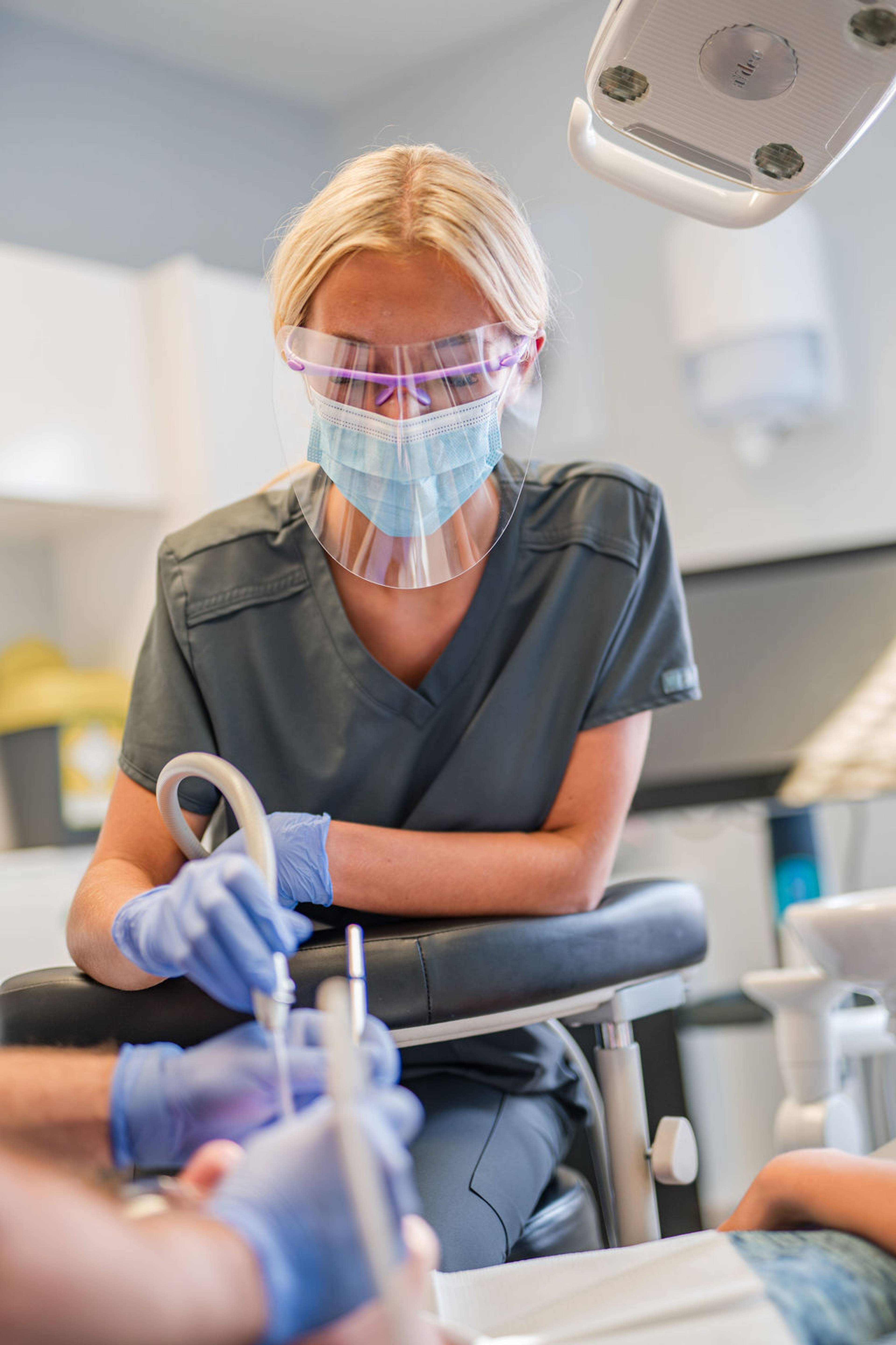 Dental professional assisting during a general dentistry treatment, using protective equipment and clinical instruments in a modern dental surgery.