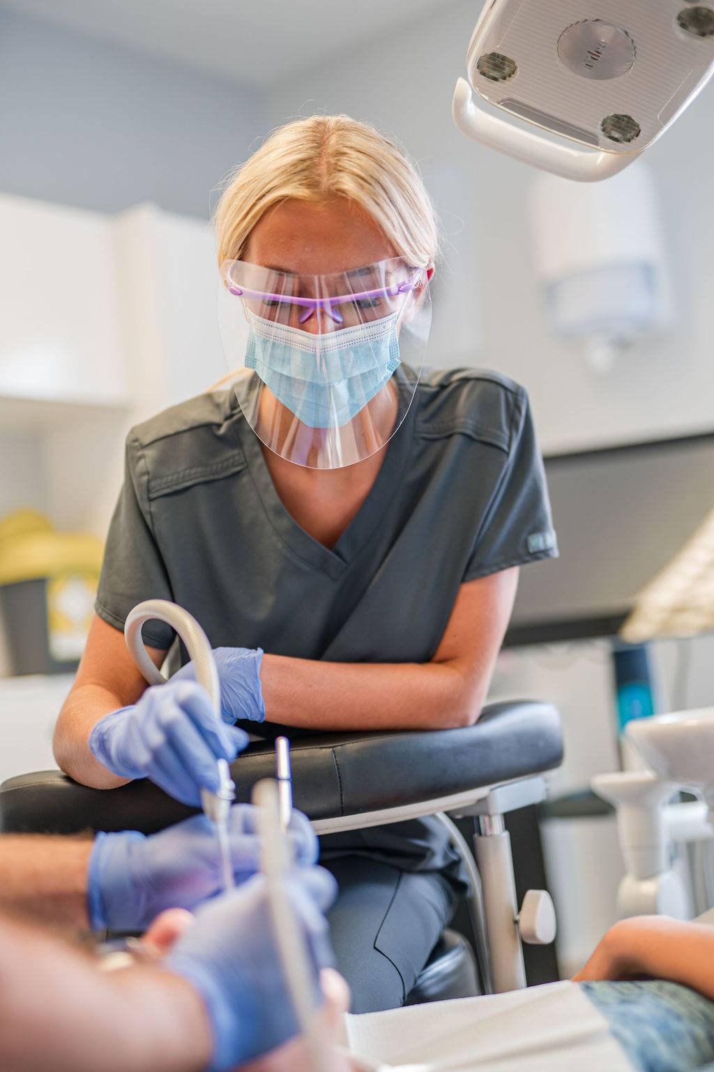 Dental professional assisting during a general dentistry treatment, using protective equipment and clinical instruments in a modern dental surgery.