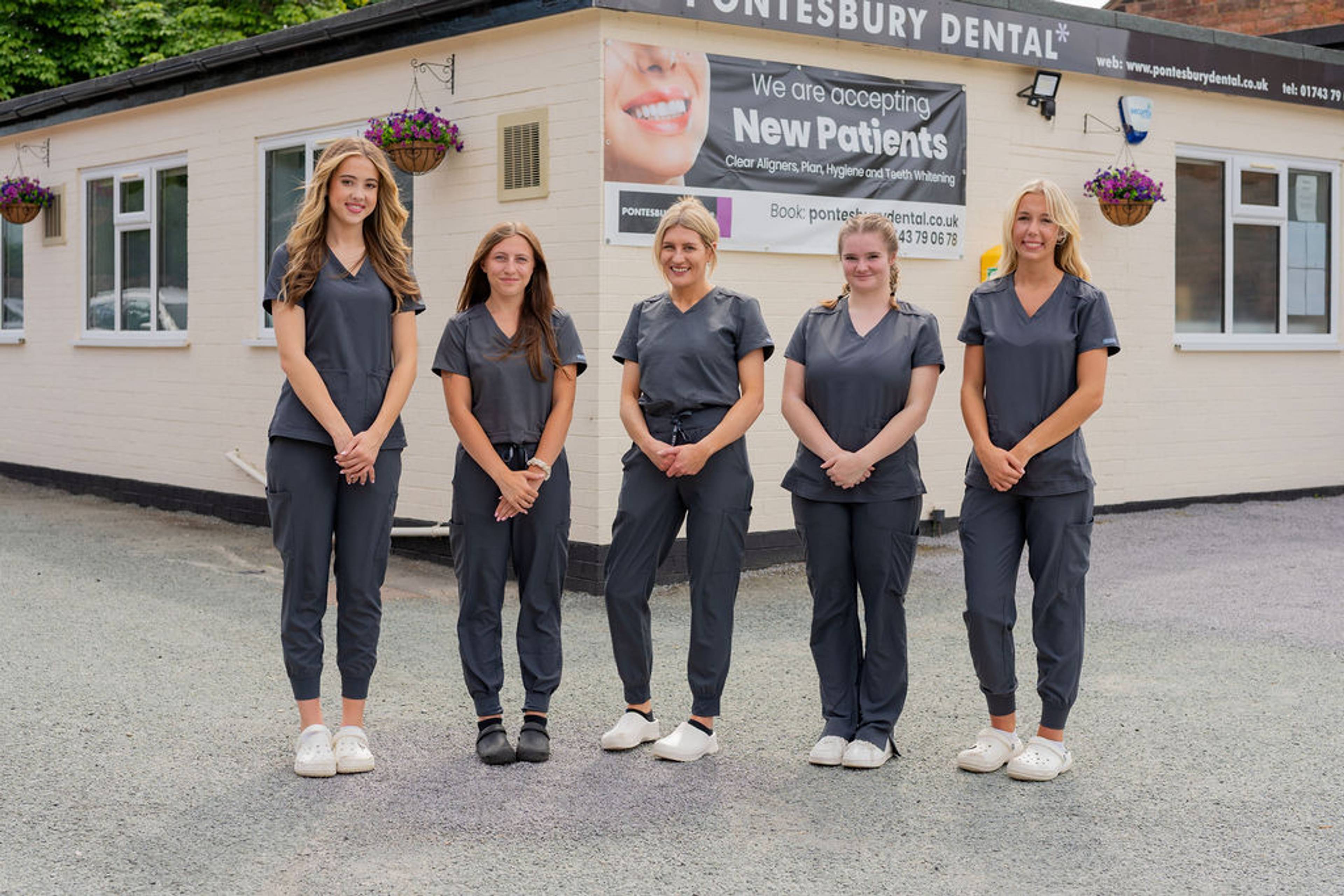 Four dental practice team members standing outside a dental clinic building in professional clinical uniforms.