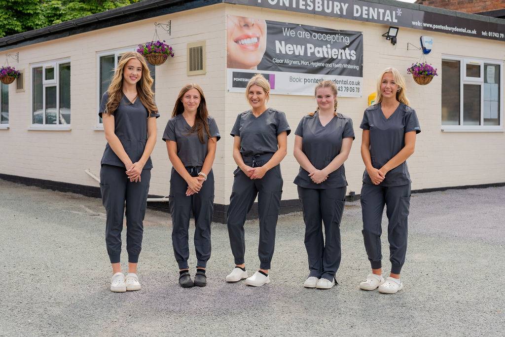 Four dental practice team members standing outside a dental clinic building in professional clinical uniforms.
