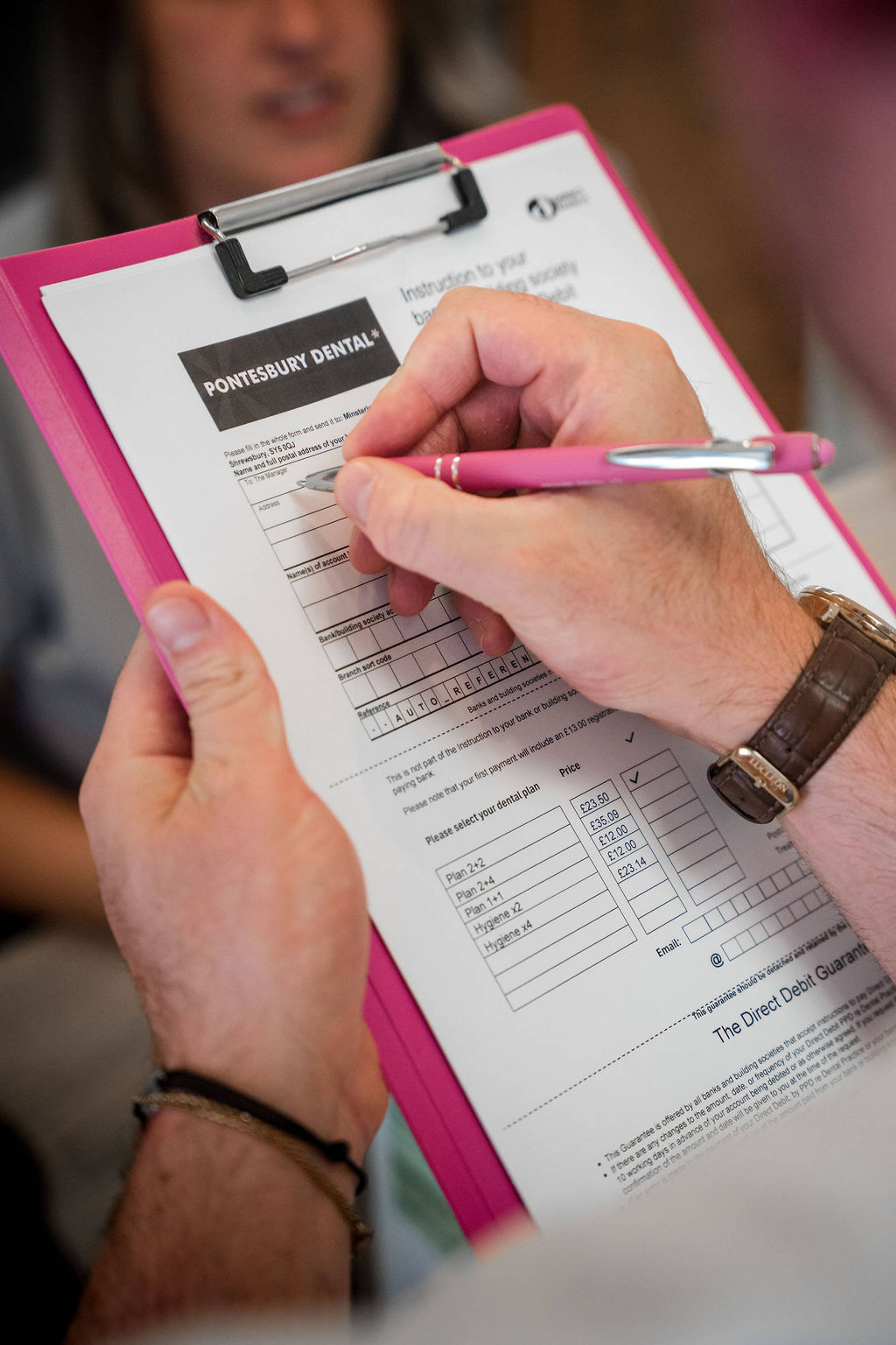 Patient completing a dental practice registration or payment form on a clipboard at reception.