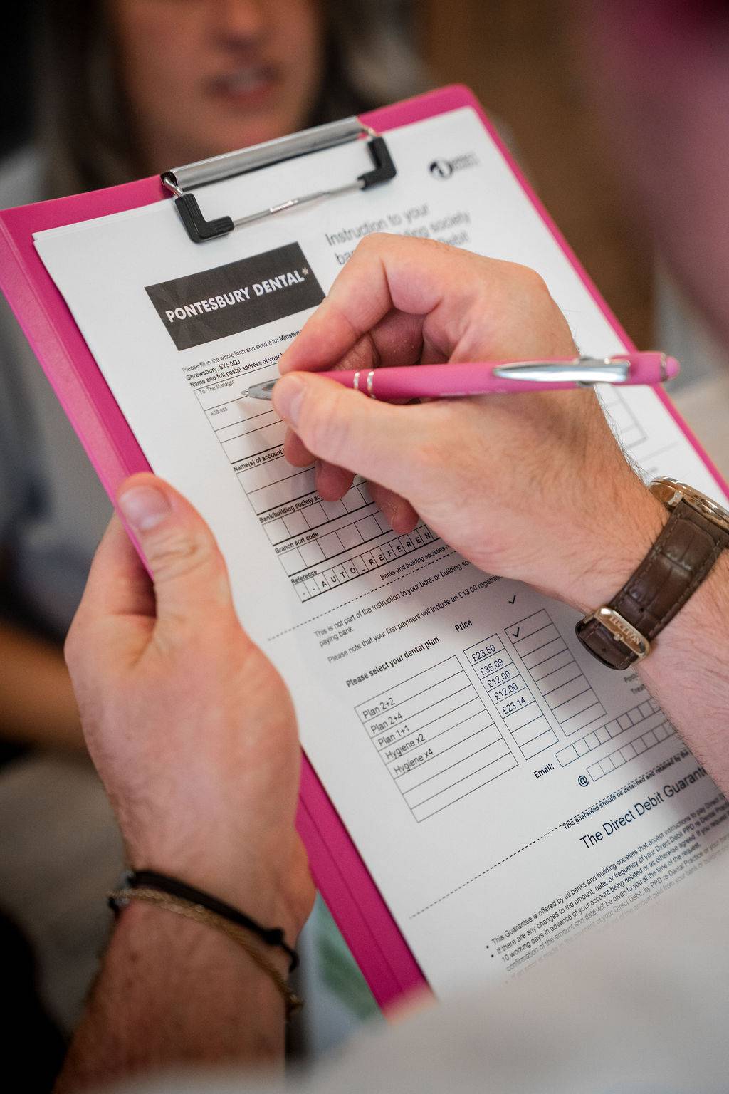 Patient completing a dental practice registration or payment form on a clipboard at reception.