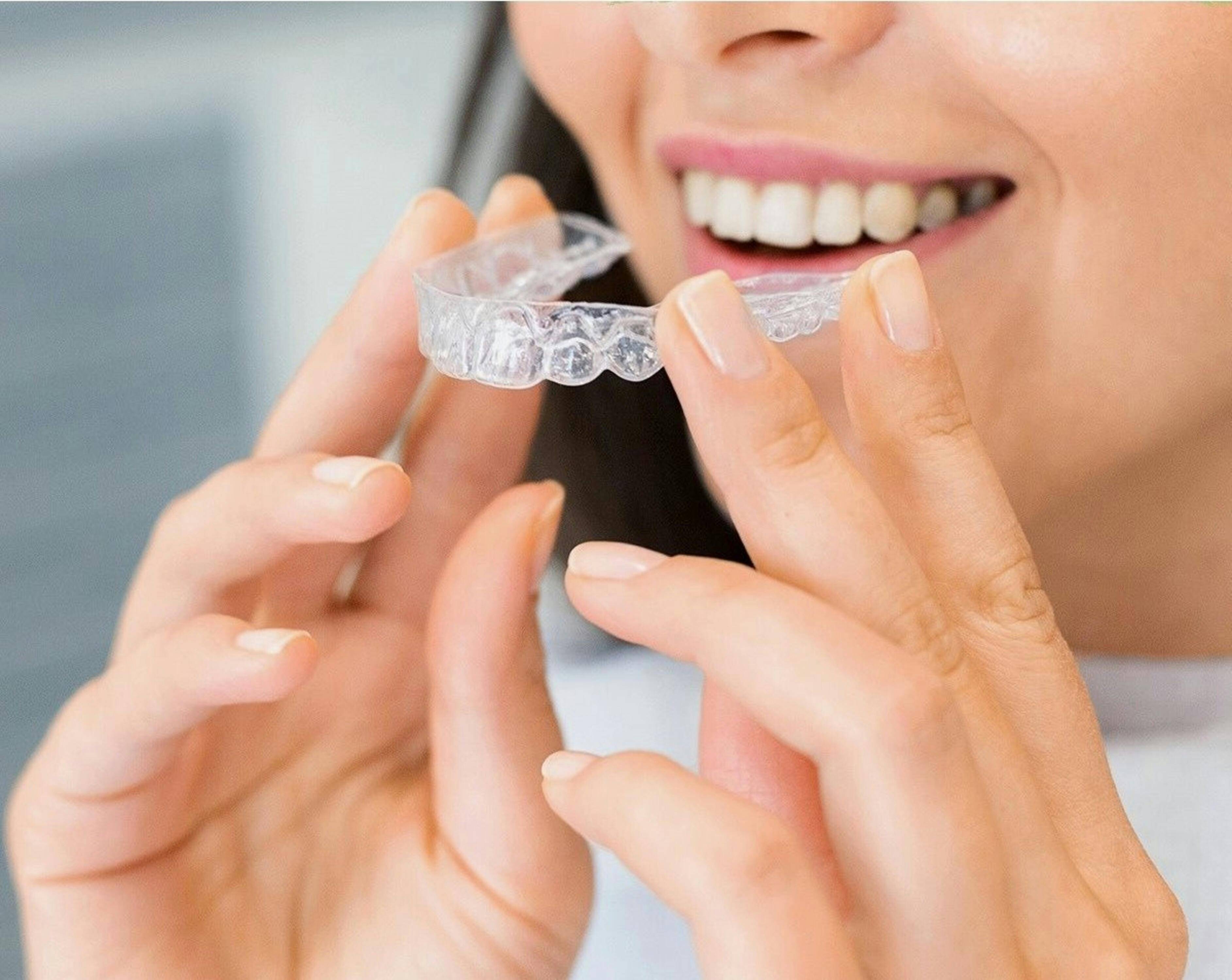 Person holding a clear removable aligner in front of their teeth before placing it into their mouth.
