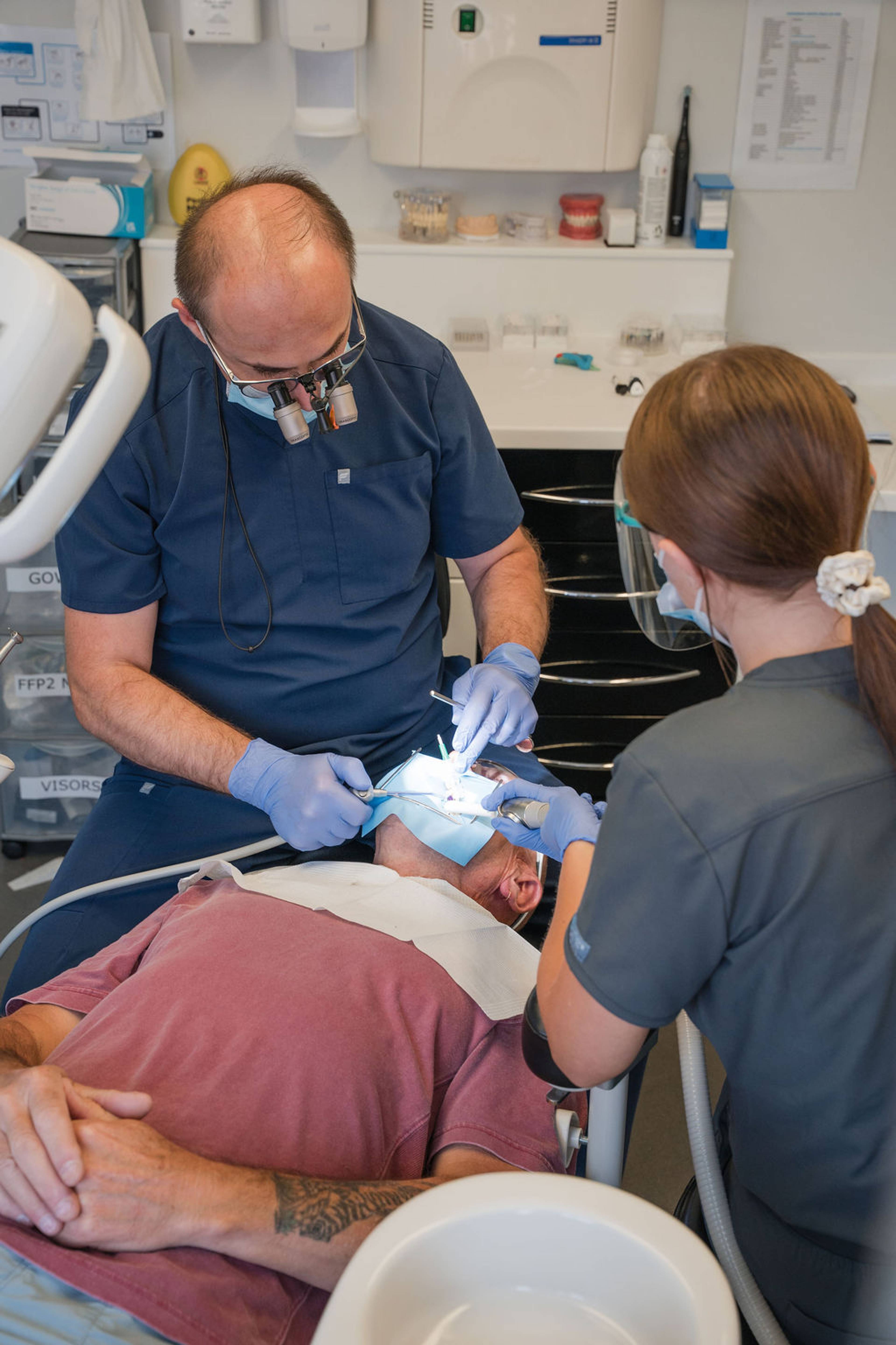 Dental professionals performing a dental procedure on a patient reclining in a treatment chair.