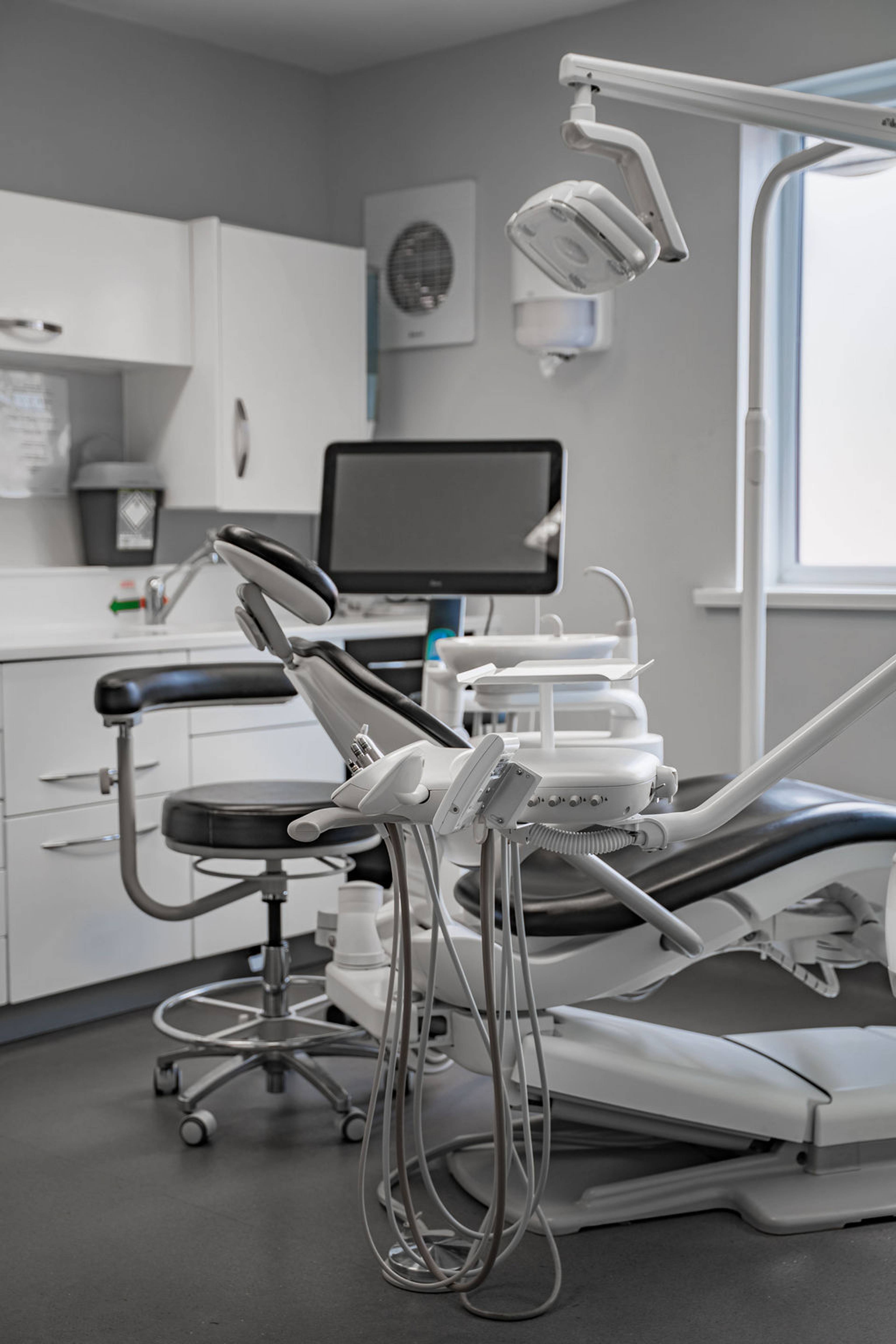 Modern dental treatment room with a dental chair, examination light, computer monitor, and dental equipment prepared for patient care.