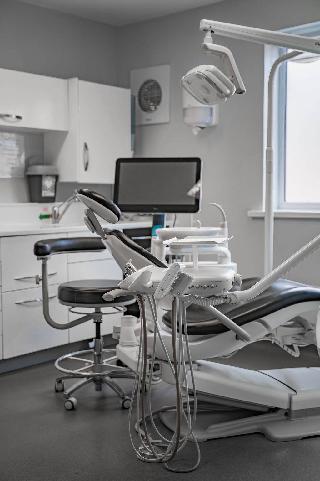 Modern dental treatment room with a dental chair, examination light, computer monitor, and dental equipment prepared for patient care.