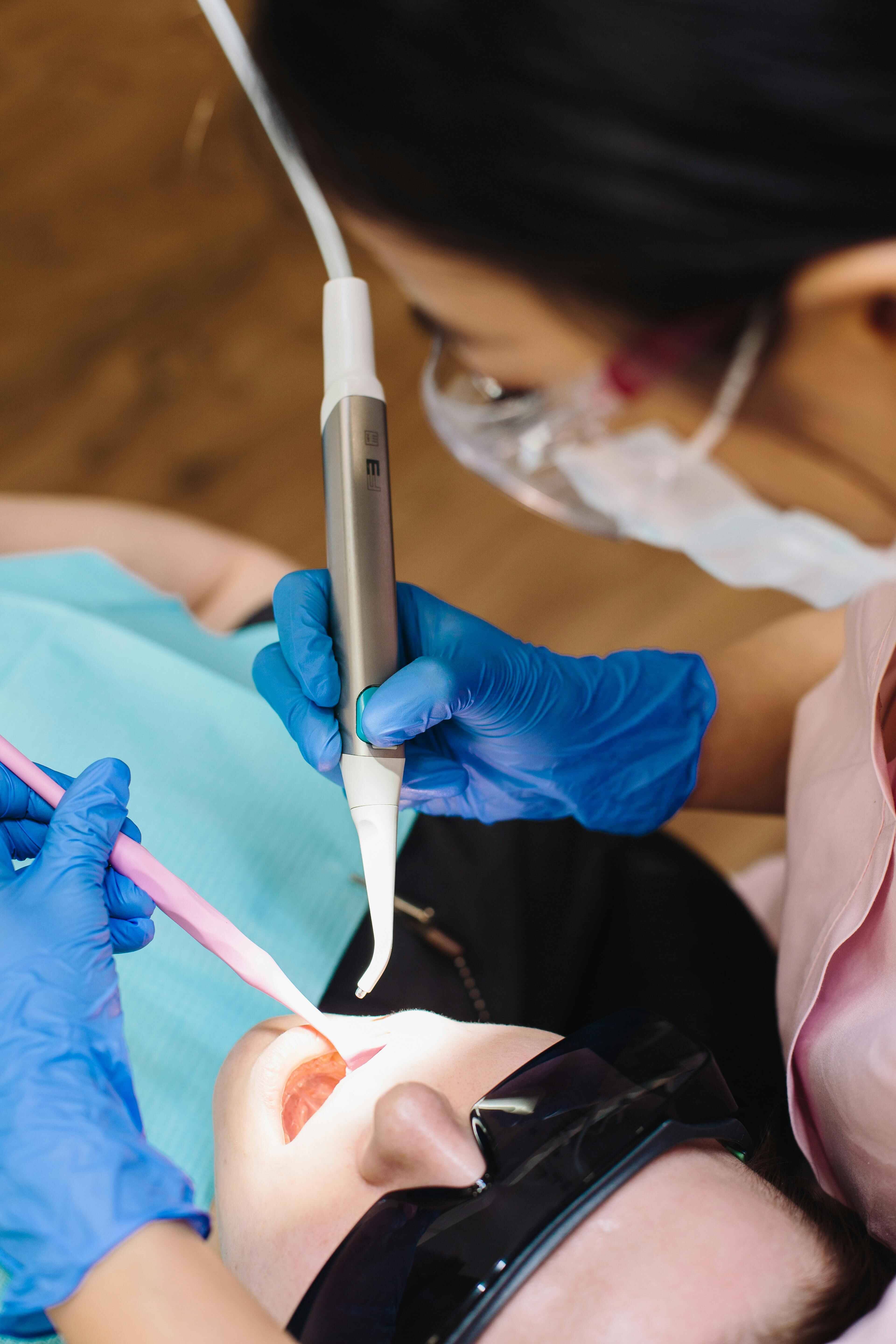 Dental professional using an ultrasonic scaler to clean a patient's teeth during a hygiene appointment.