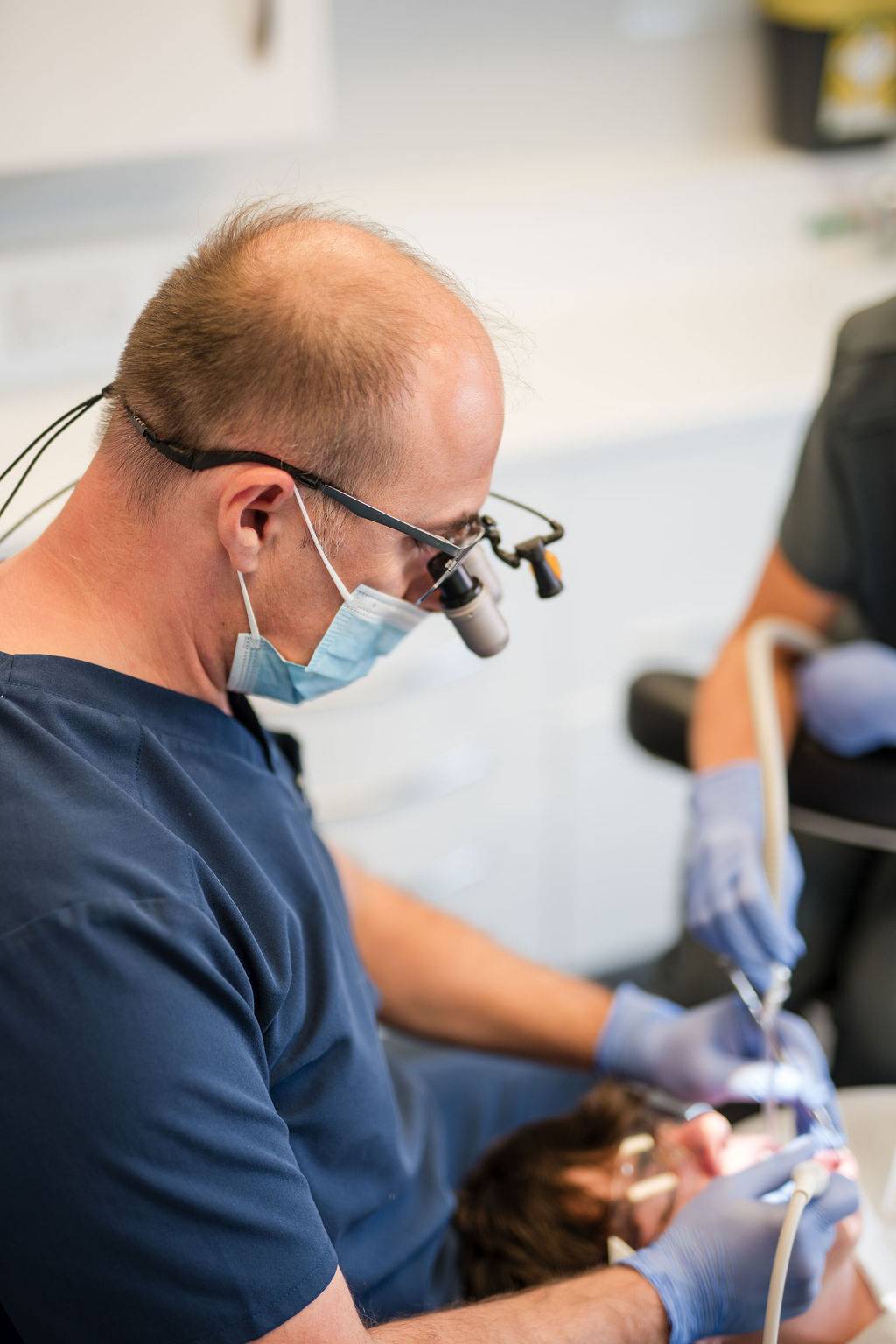 Dentist performing a general dentistry procedure using magnification loupes and specialised dental instruments in a modern clinical treatment room.