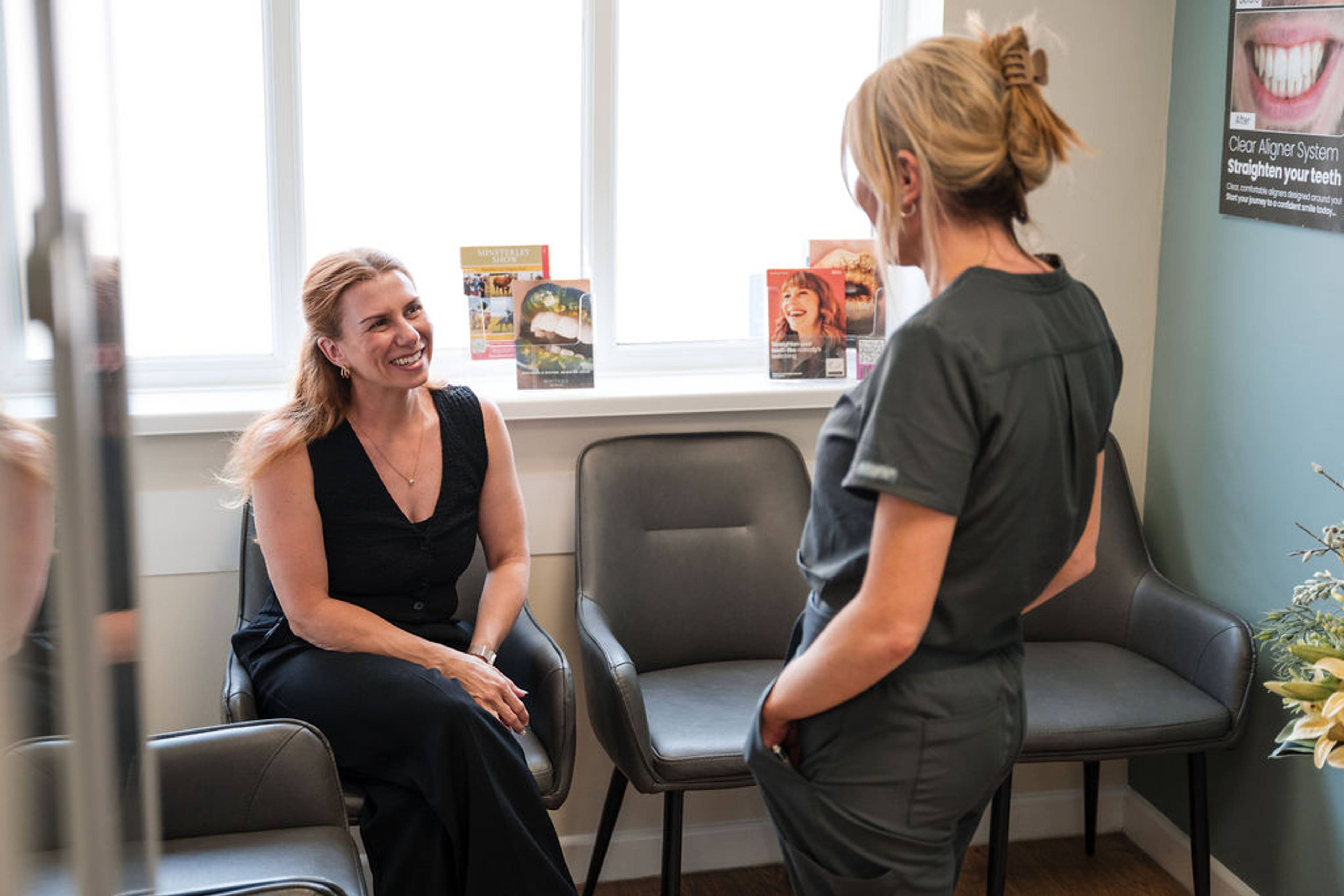 Dental team member speaking with a patient in a dental clinic waiting area beside a display of oral care products.
