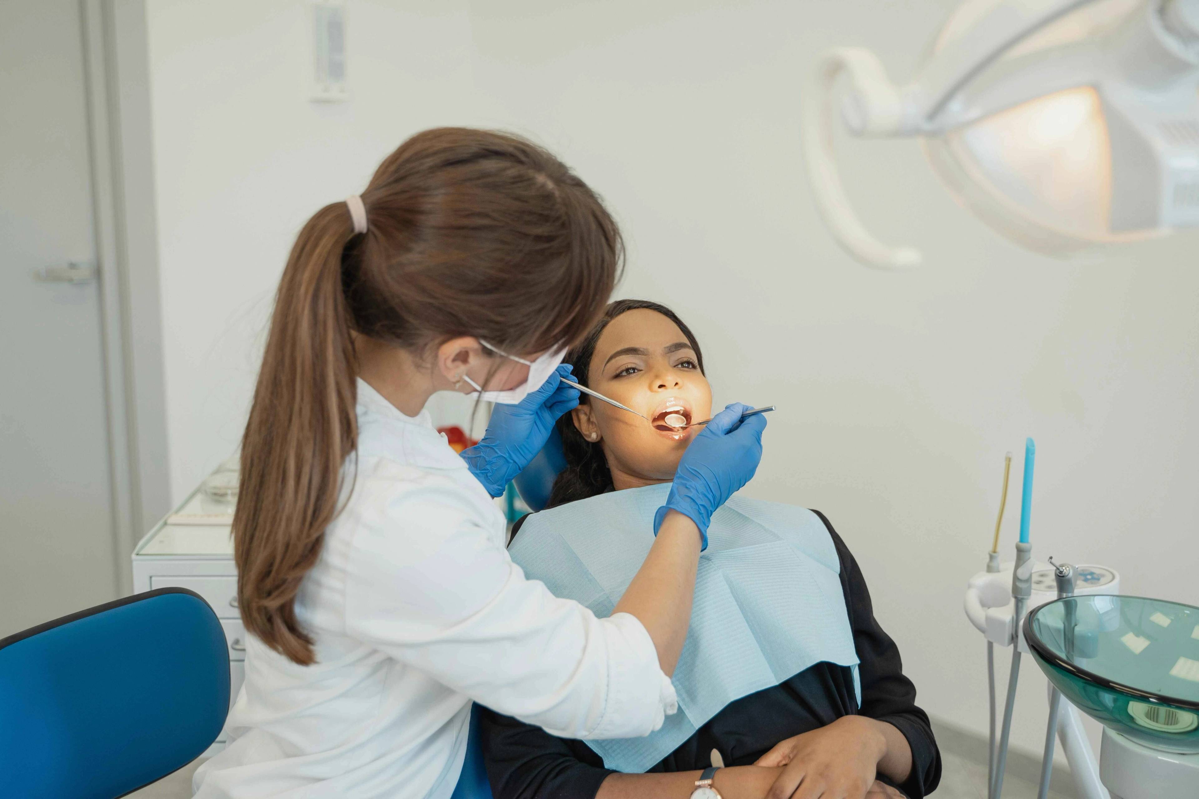 Dental professional performing an oral examination on a patient seated in a dental chair using a dental mirror and examination instrument.