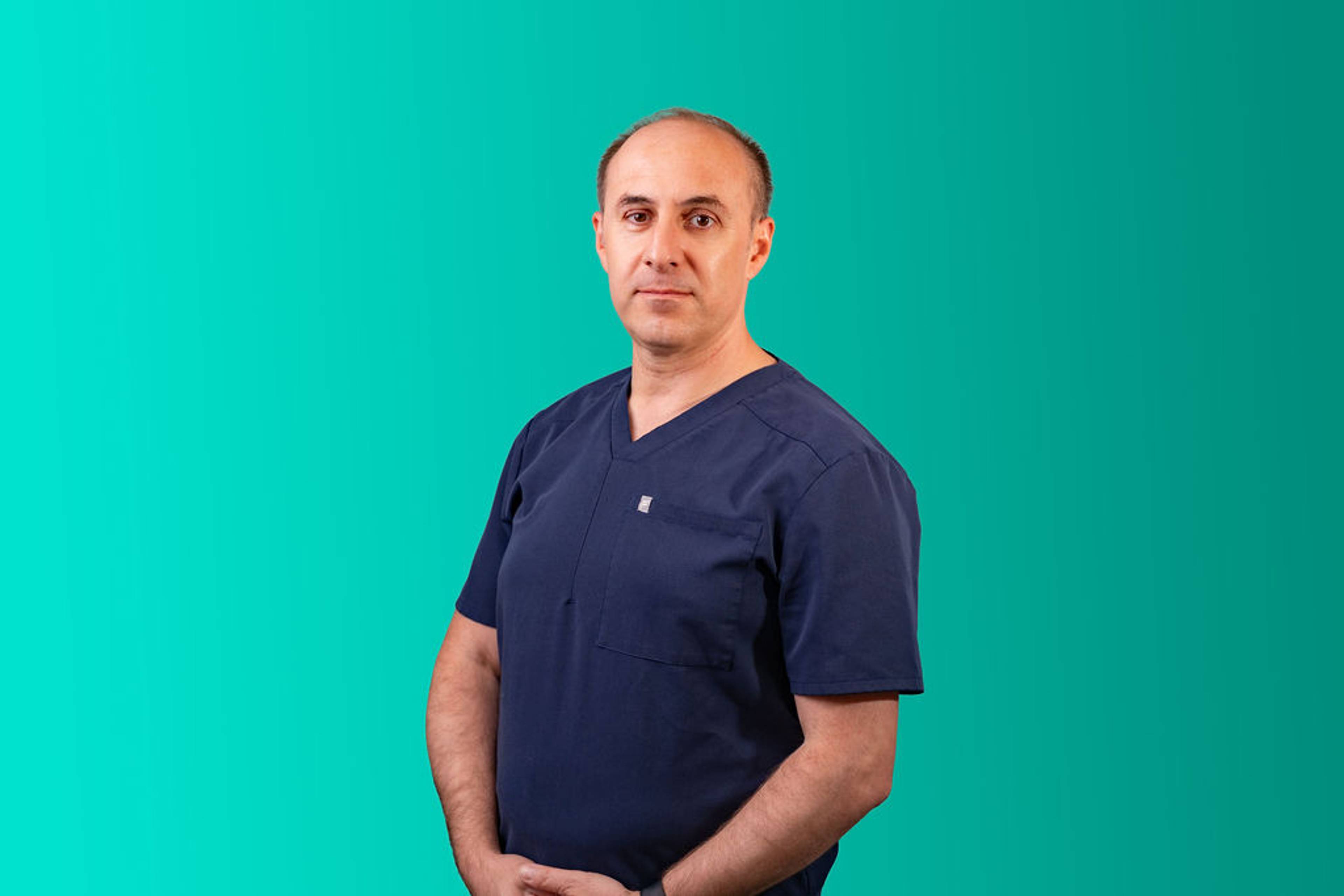 Professional headshot of a dental practitioner in navy scrubs standing against a turquoise background.