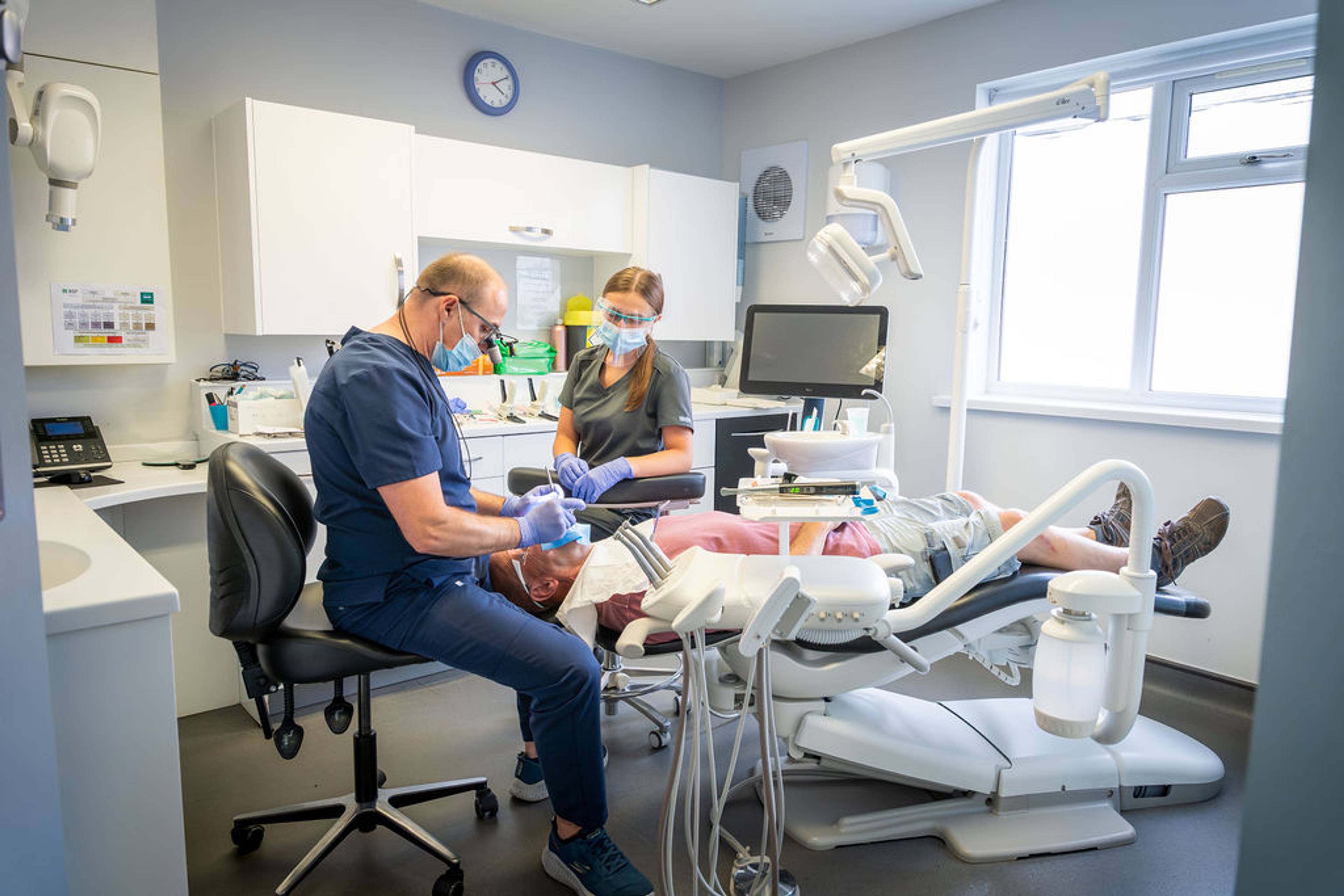 Modern dental treatment room with a patient receiving care from two dental professionals surrounded by advanced dental equipment.