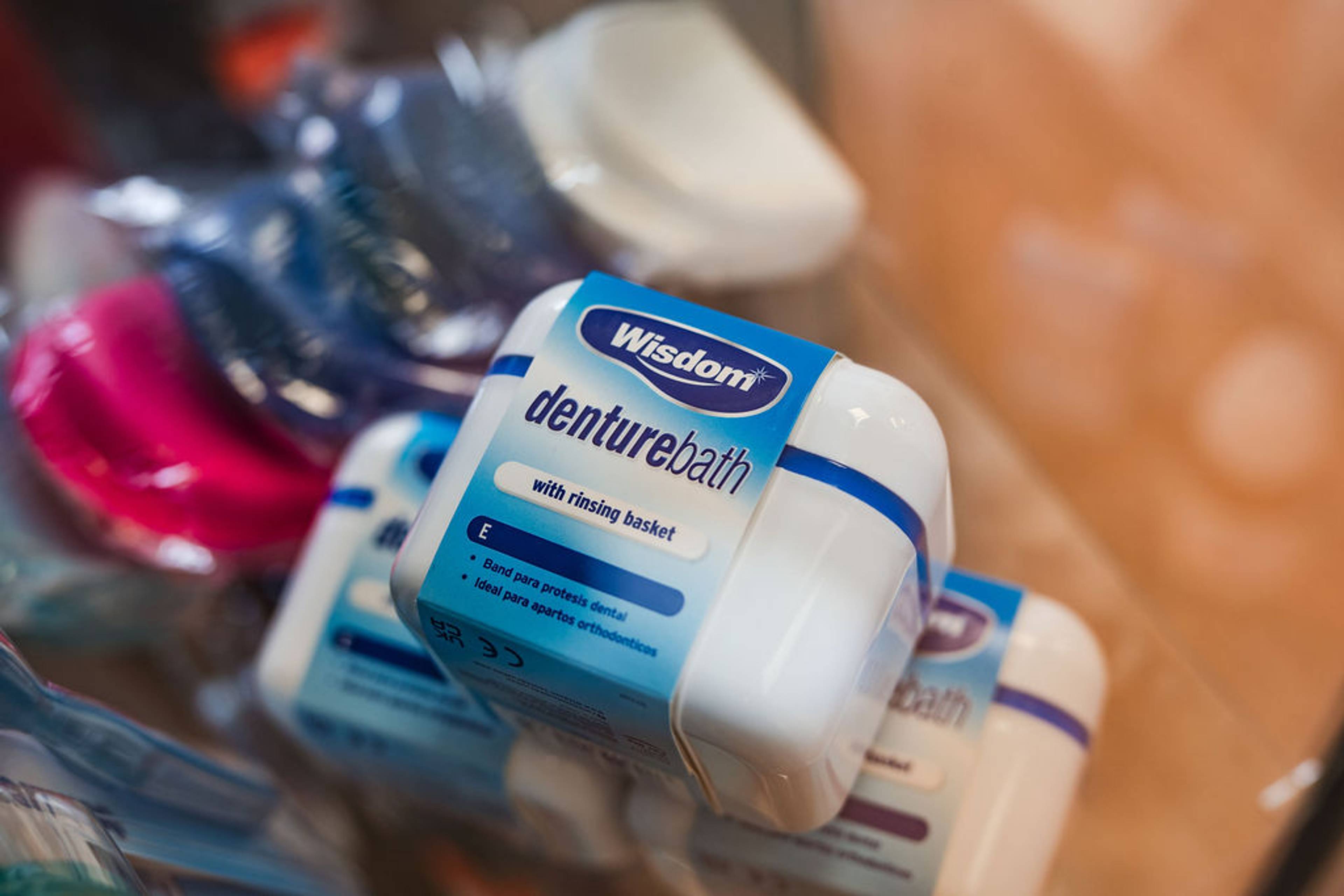 Container of denture cleaning accessories displayed in a dental practice, including a denture bath with rinsing basket.