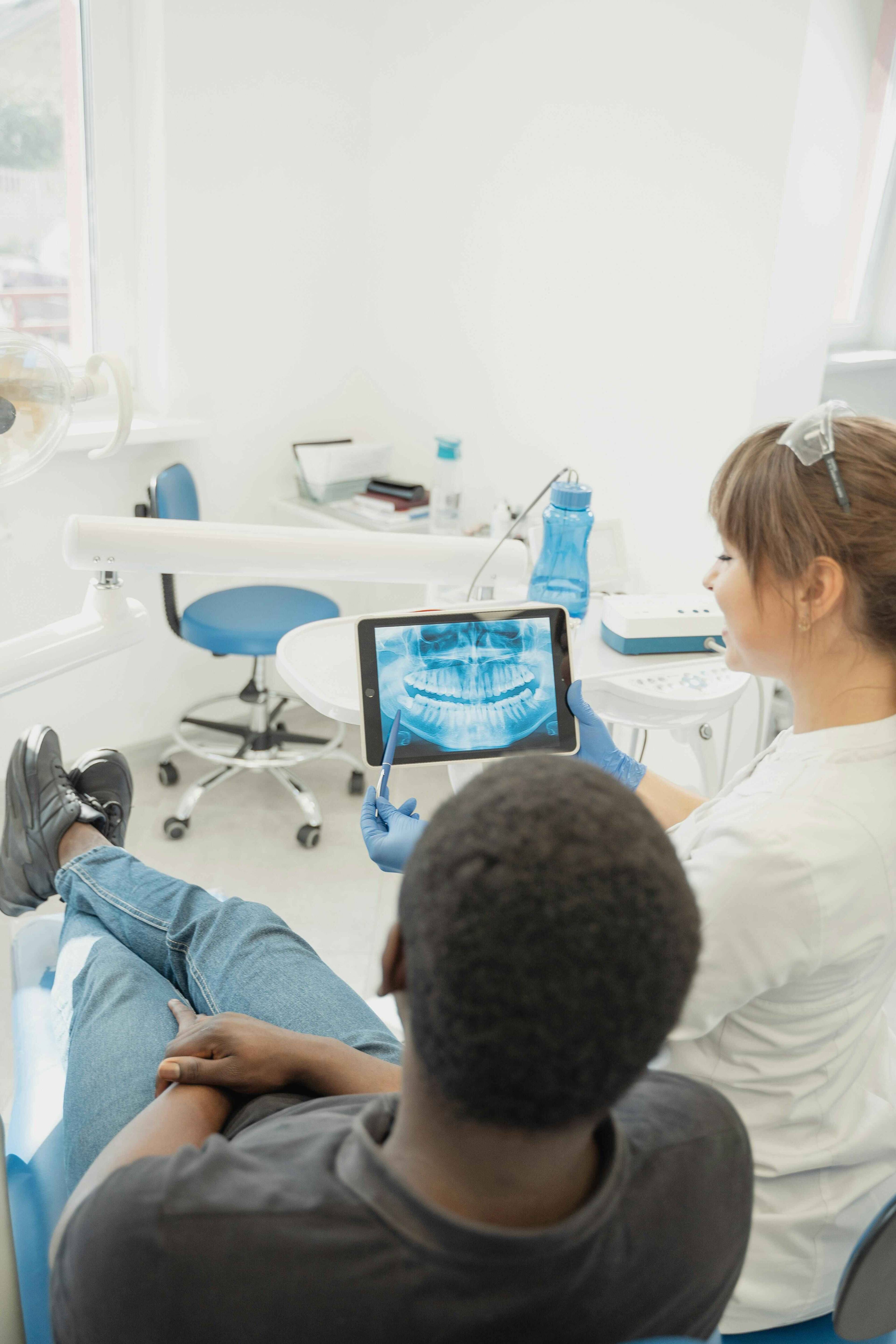 Dental professional reviewing a patient's panoramic dental X-ray on a tablet during a consultation in a treatment room.